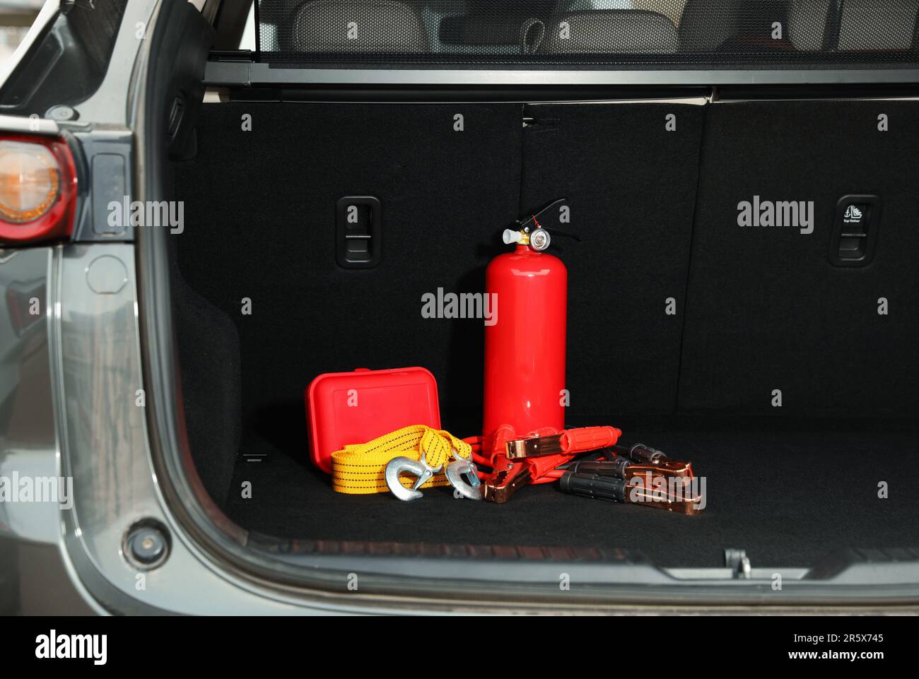 Red fire extinguisher, battery jumper cables, towing strap and first aid kit in trunk. Car