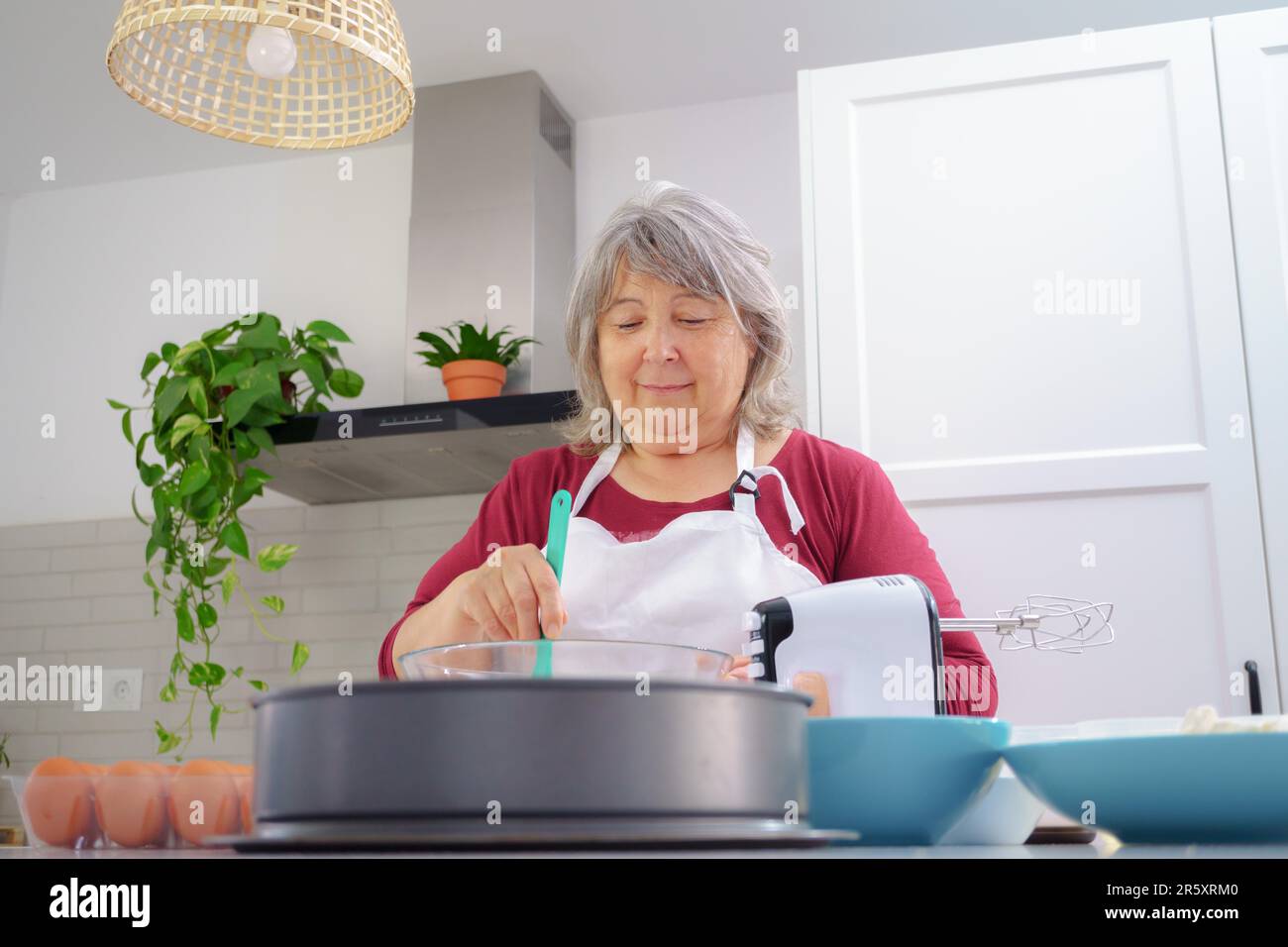 Female cook in white apron beating eggs in a bowl with a spatula Stock Photo