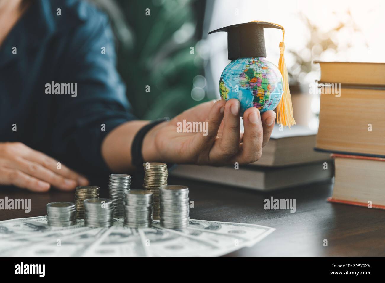 Hand holding graduation cap on globe with stack coin. Concept of saving money for a scholarship to study abroad at a university level. Financial plann Stock Photo