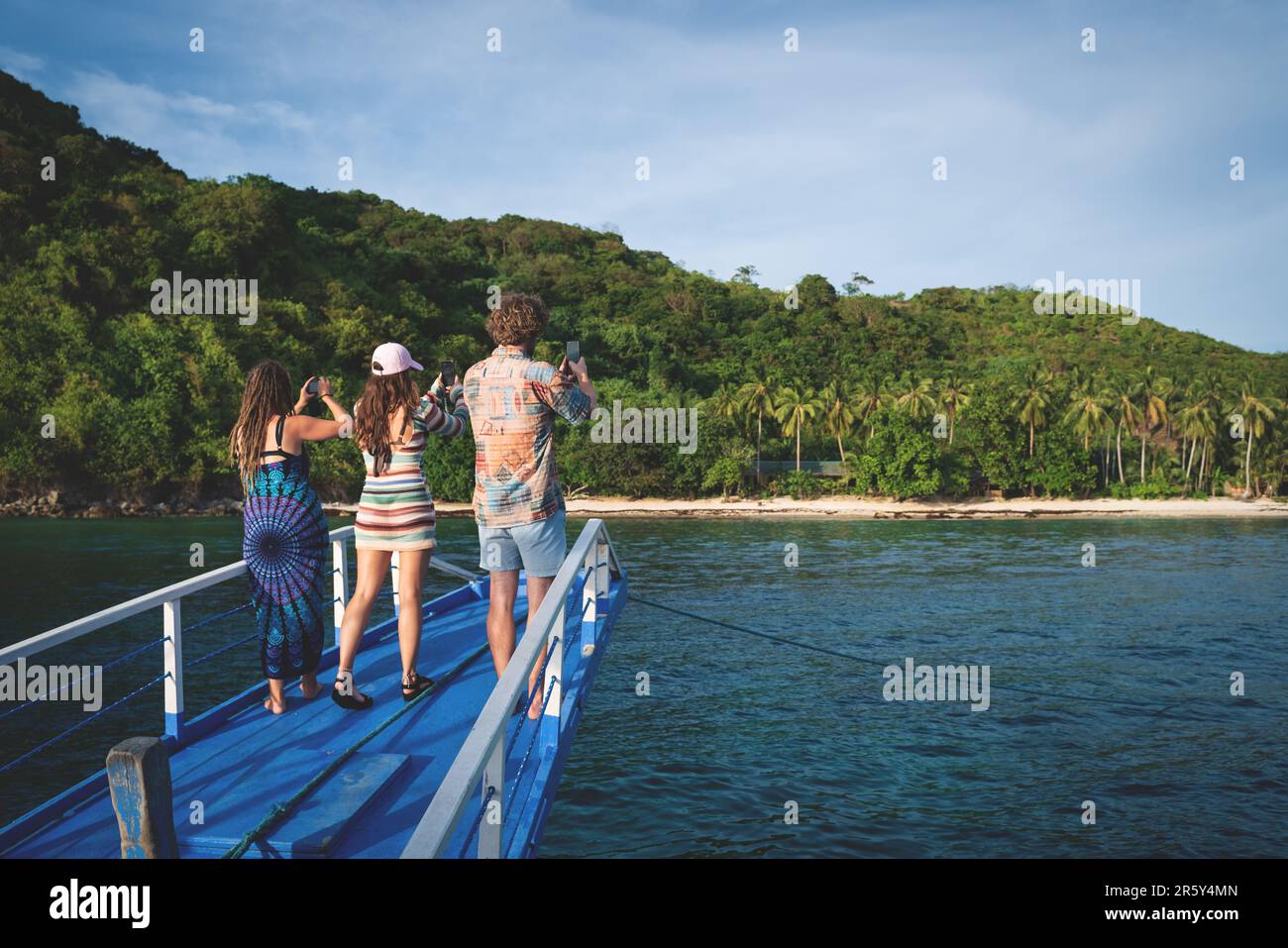 Palawan, Philippines - 28 February 2023: Three tourists holding their smartphones to make a picture of beautiful sunny beach Stock Photo
