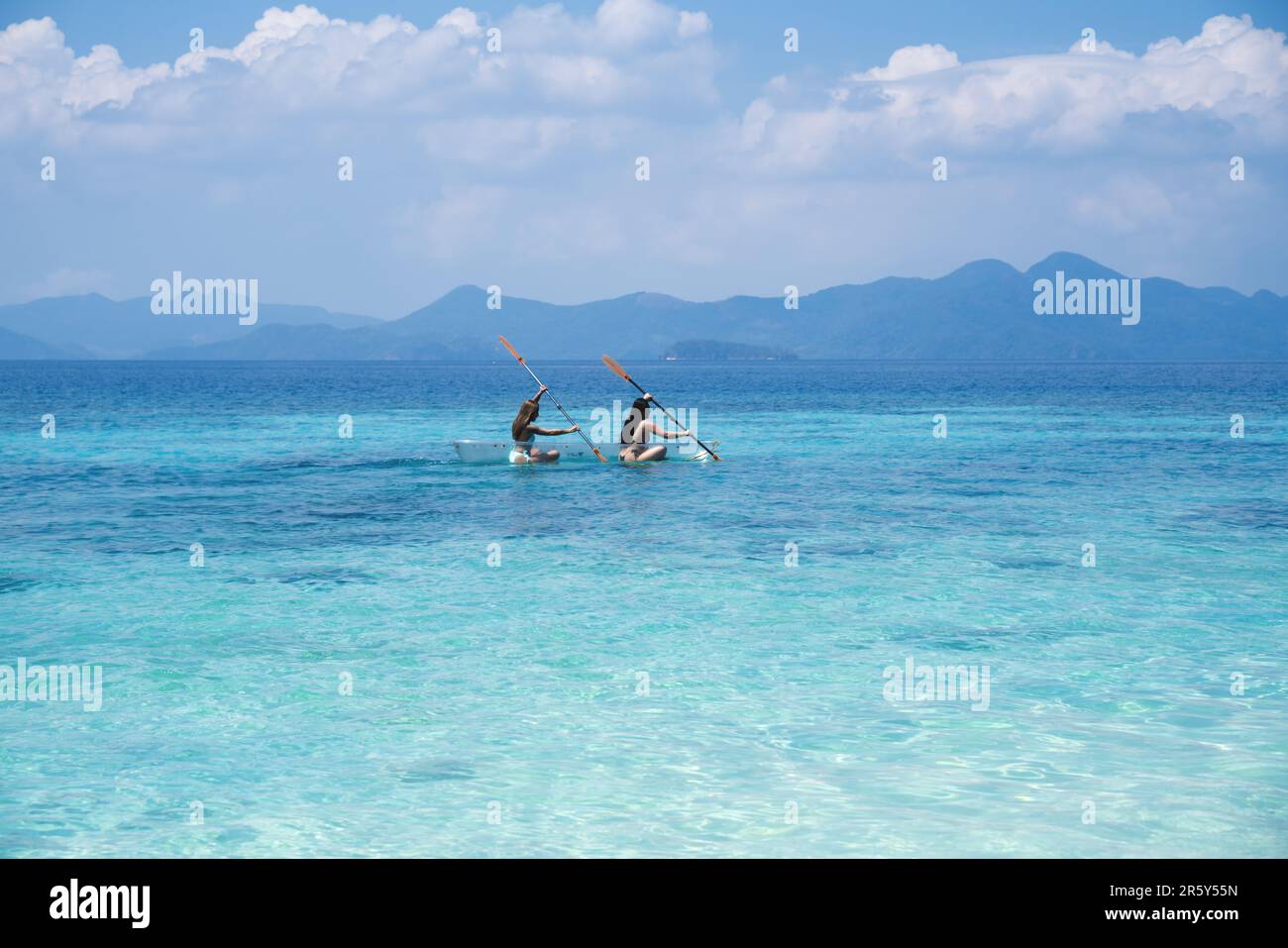 Bullog Island, Coron, Philippines - 24 February 2023: Two female tourists paddling in a transparent kayak in clear turquoise water with islands in the Stock Photo
