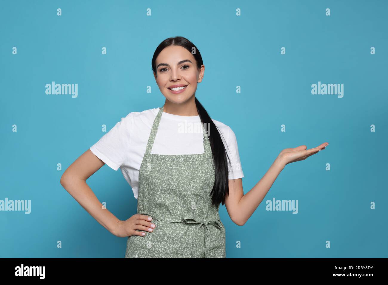 Young woman in grey apron on light blue background Stock Photo - Alamy