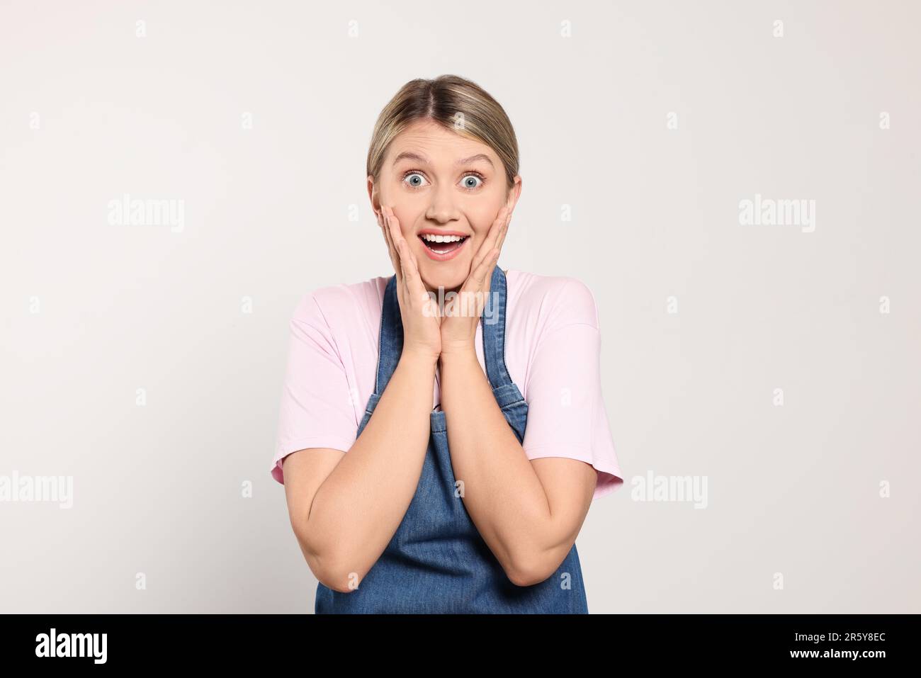 Beautiful young woman in denim apron on light grey background Stock ...