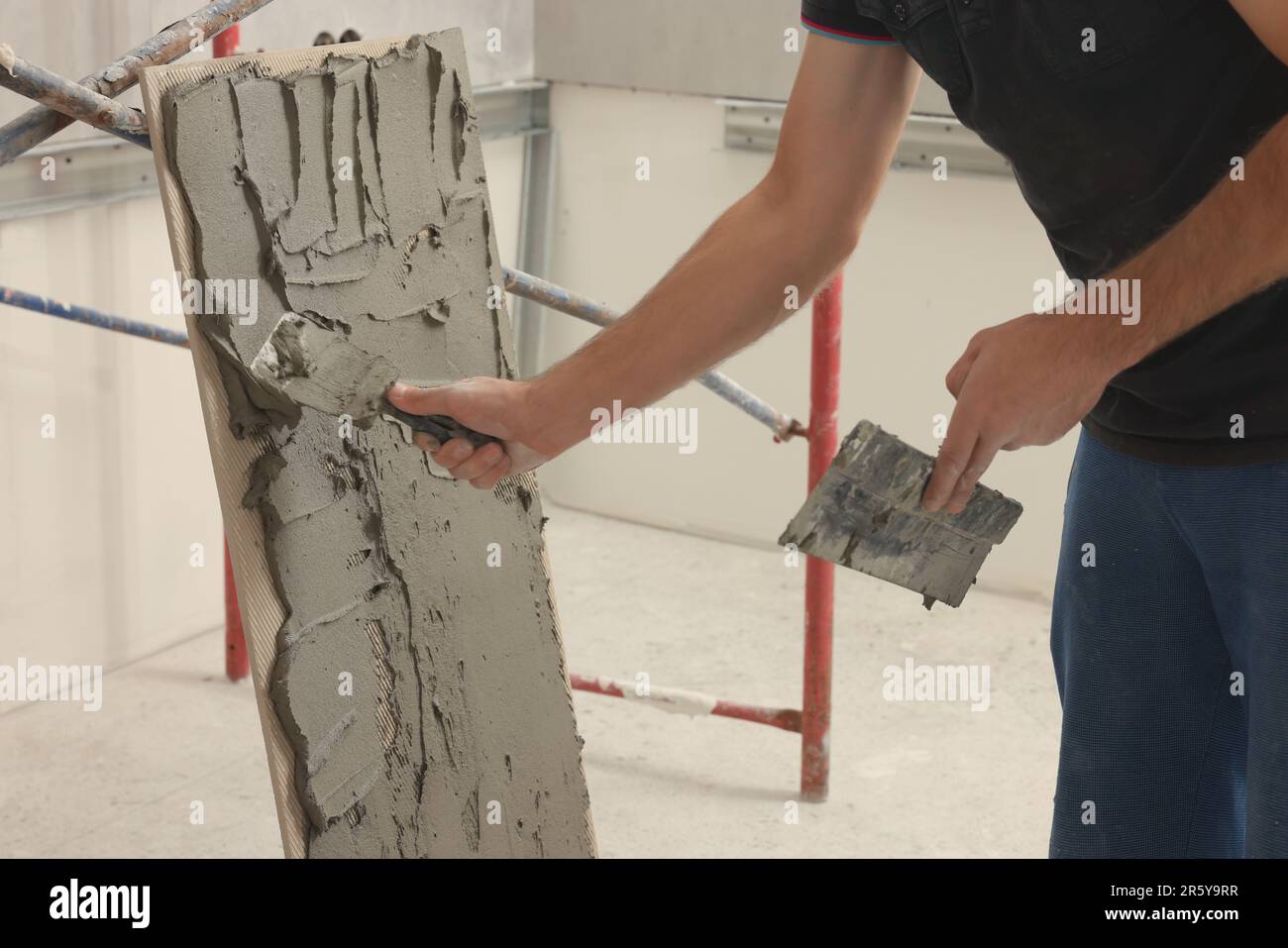 Worker spreading adhesive mix over tile with spatula, closeup Stock Photo