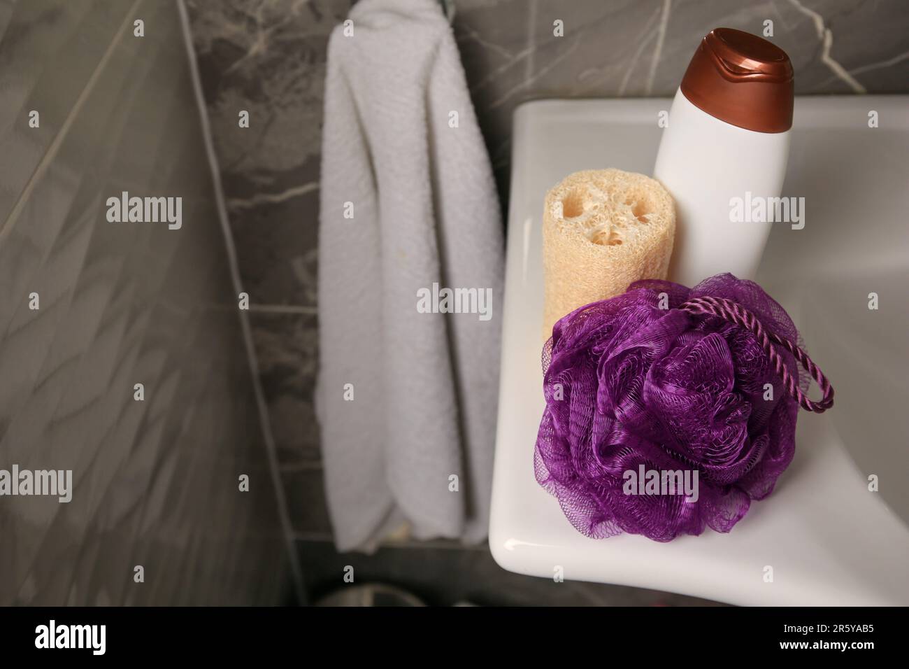 Purple shower puff, loofah sponge and bottle of body wash gel on sink