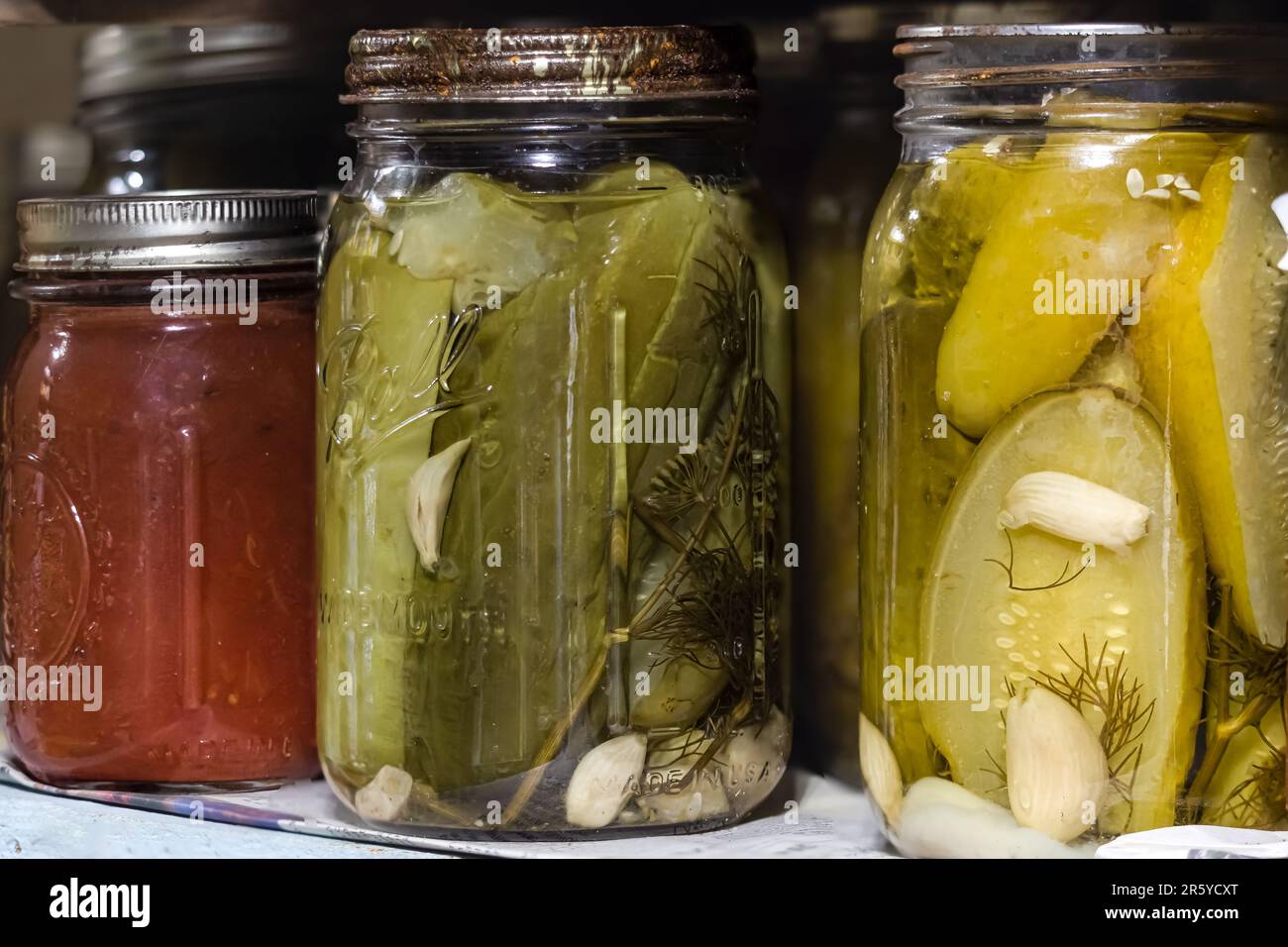 Two canning jars filled with green pickles and garlic cloves and one