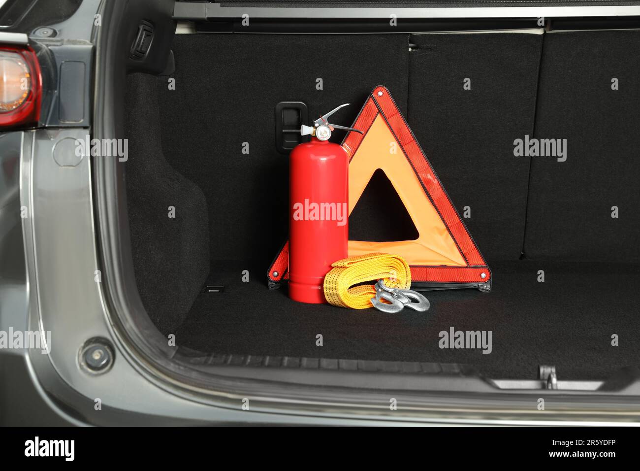 Red fire extinguisher, towing strap and foldable emergency warning triangle in trunk. Car safety