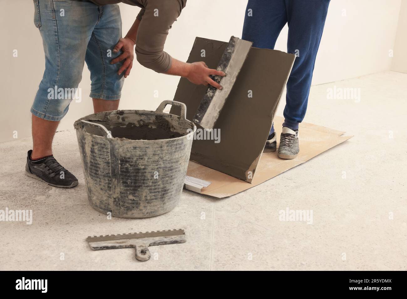 Worker spreading adhesive mix over tile with spatula, closeup Stock Photo
