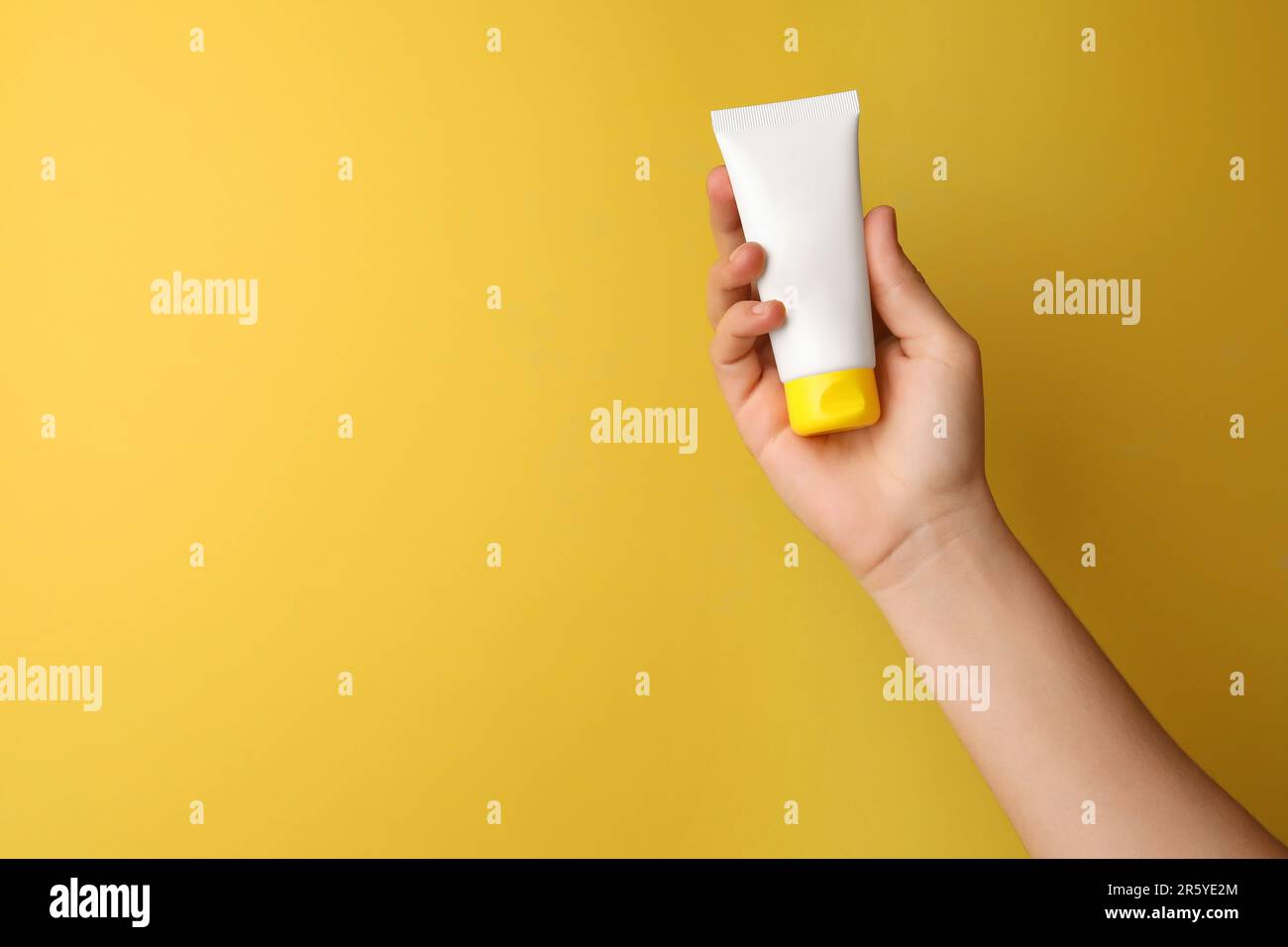Woman holding tube of face cream on yellow background, closeup. Space