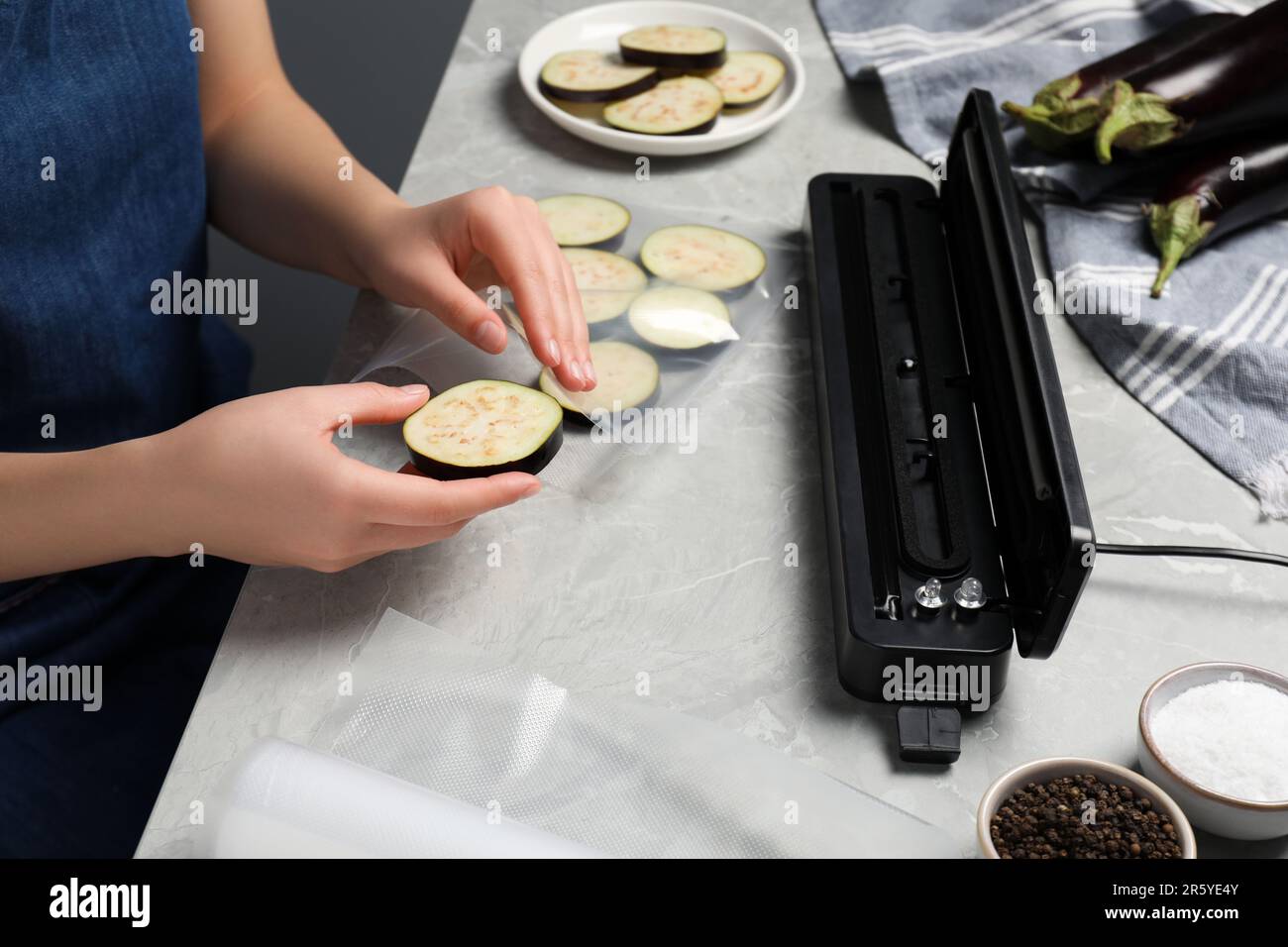 Woman packing cut eggplant into plastic bag using vacuum sealer on