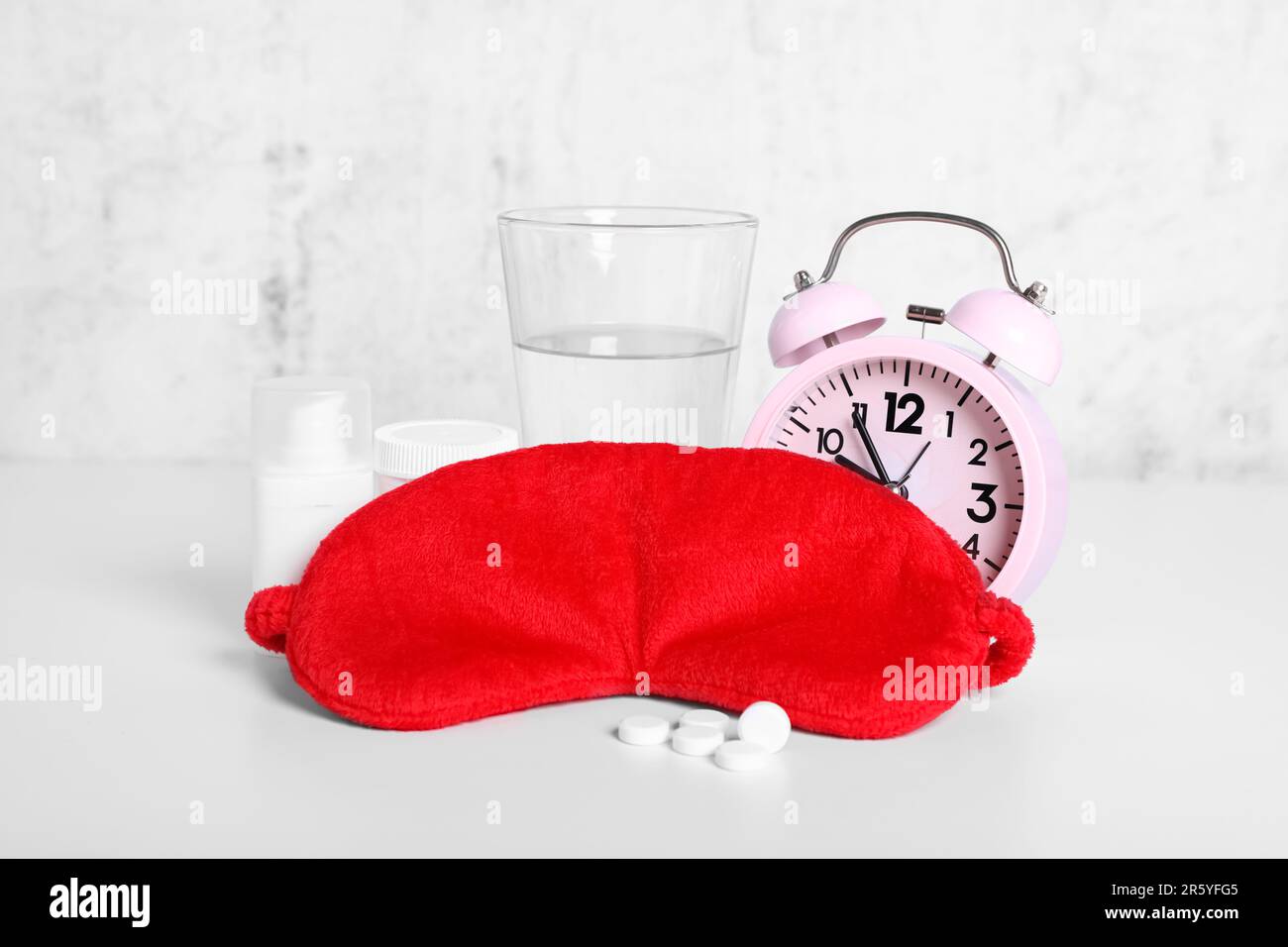 Red sleep mask, glass of water, pills and alarm clock on white table Stock Photo