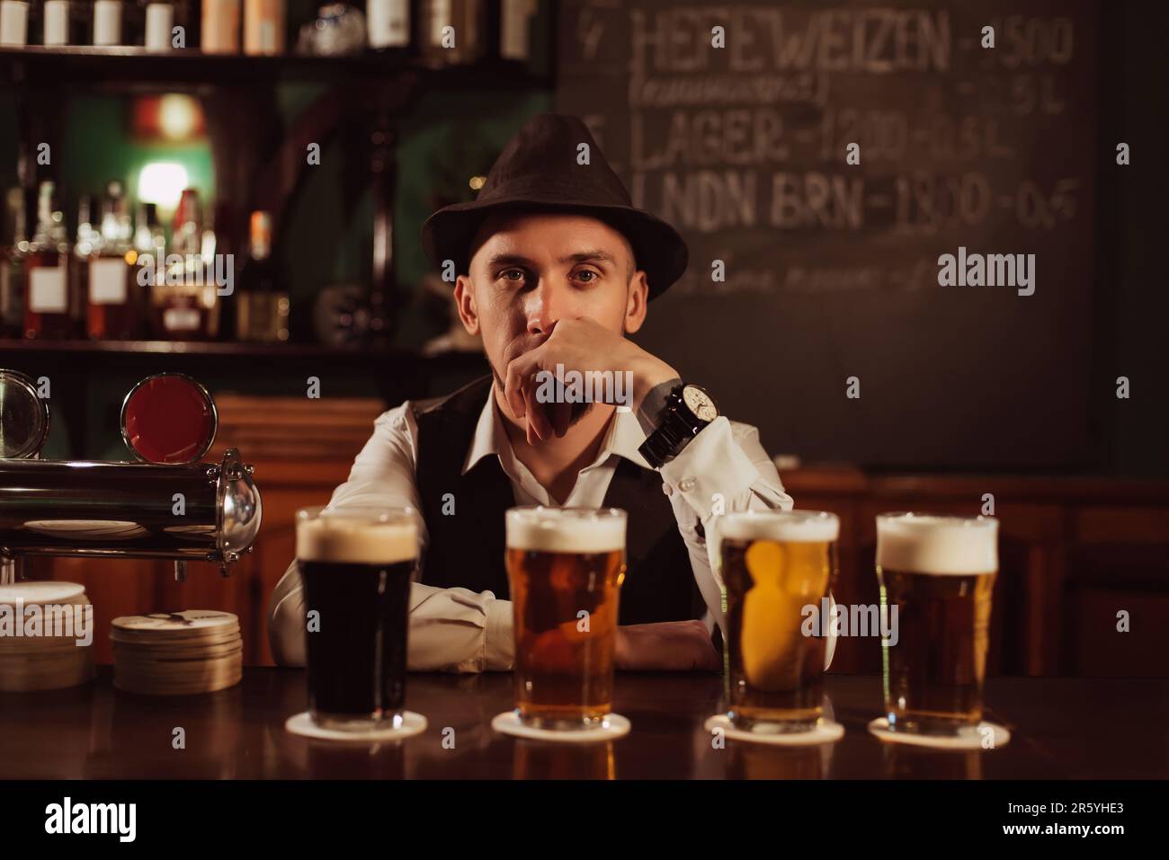 bartender in hat with a beard at bar counter with beer in glasses in