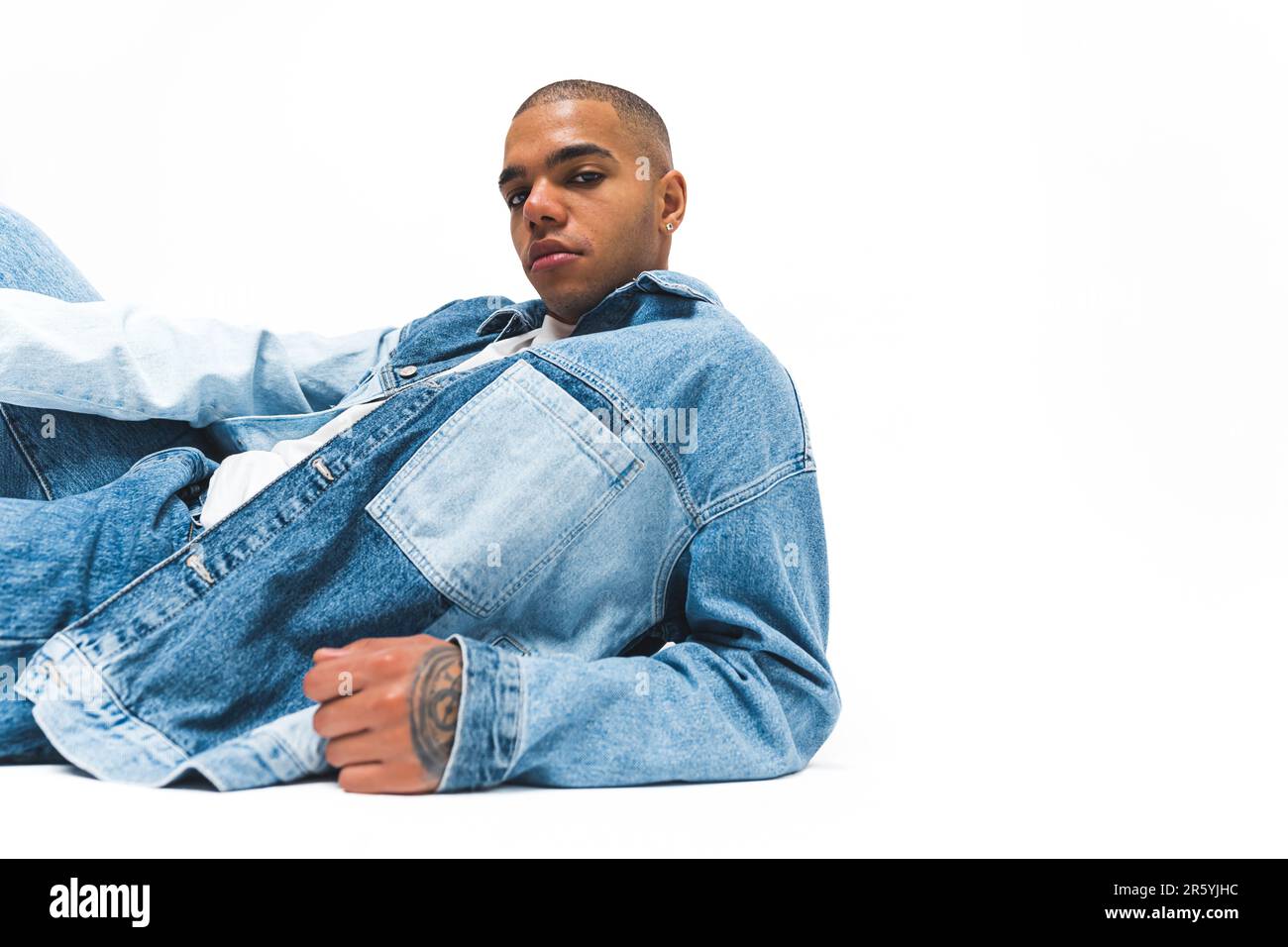 African American man with serious facial expression wearing denim jacket and jeans posing on the floor against a white background. High quality 4k footage Stock Photo