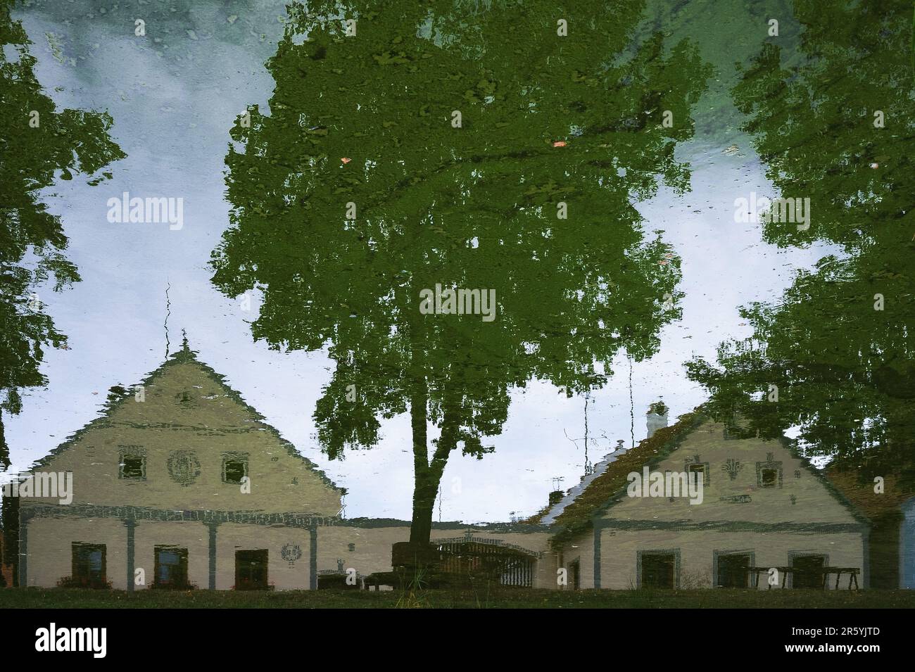 This image has been rotated by 180 degrees.  Pointed gables of properties in Holašovice, South Bohemia, Czech Republic or Czechia, reflected in the still water of a pond on the village green.  Holašovice is a well-preserved example of a traditional Central European village with a ground plan dating from the Middle Ages and a number of 1700s AD and 1800s AD vernacular buildings in a style known as South Bohemian Folk Baroque, Rural Baroque or Rustic Baroque.  In 1997 the village was included in the UNESCO World Cultural Heritage List. Stock Photo