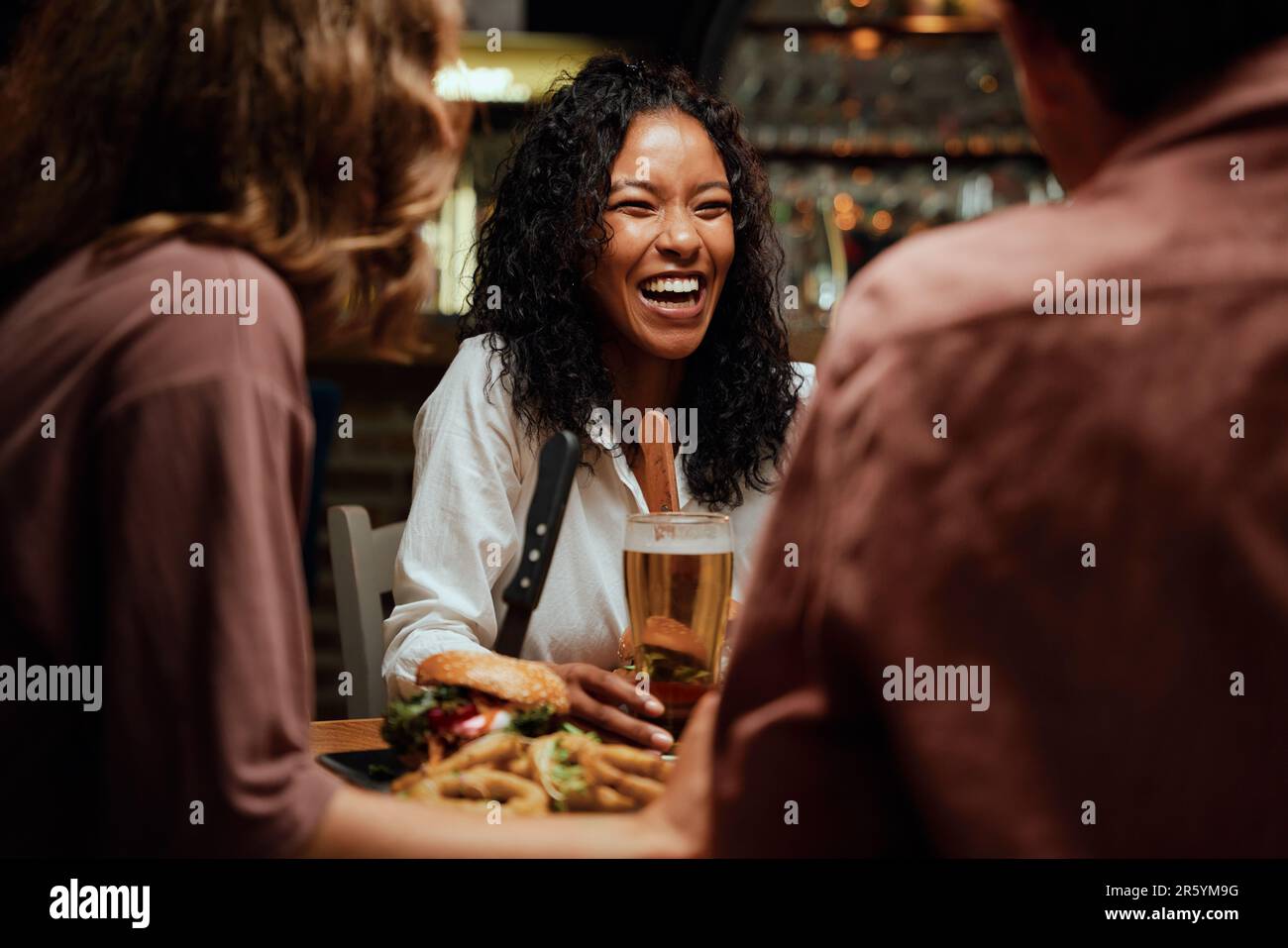 Happy young multiracial group of friends in casual clothing laughing during dinner at restaurant Stock Photo