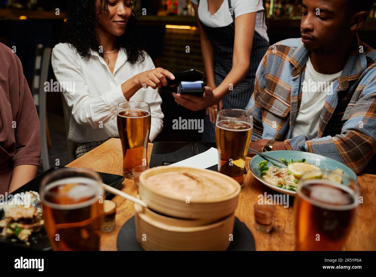 Young multiracial group of friends in casual clothing paying for dinner and drinks at bar Stock Photo