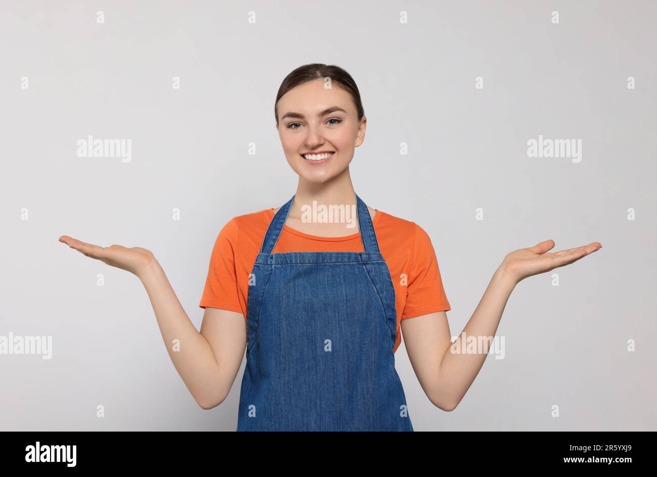 Beautiful young woman in clean denim apron on light grey background ...
