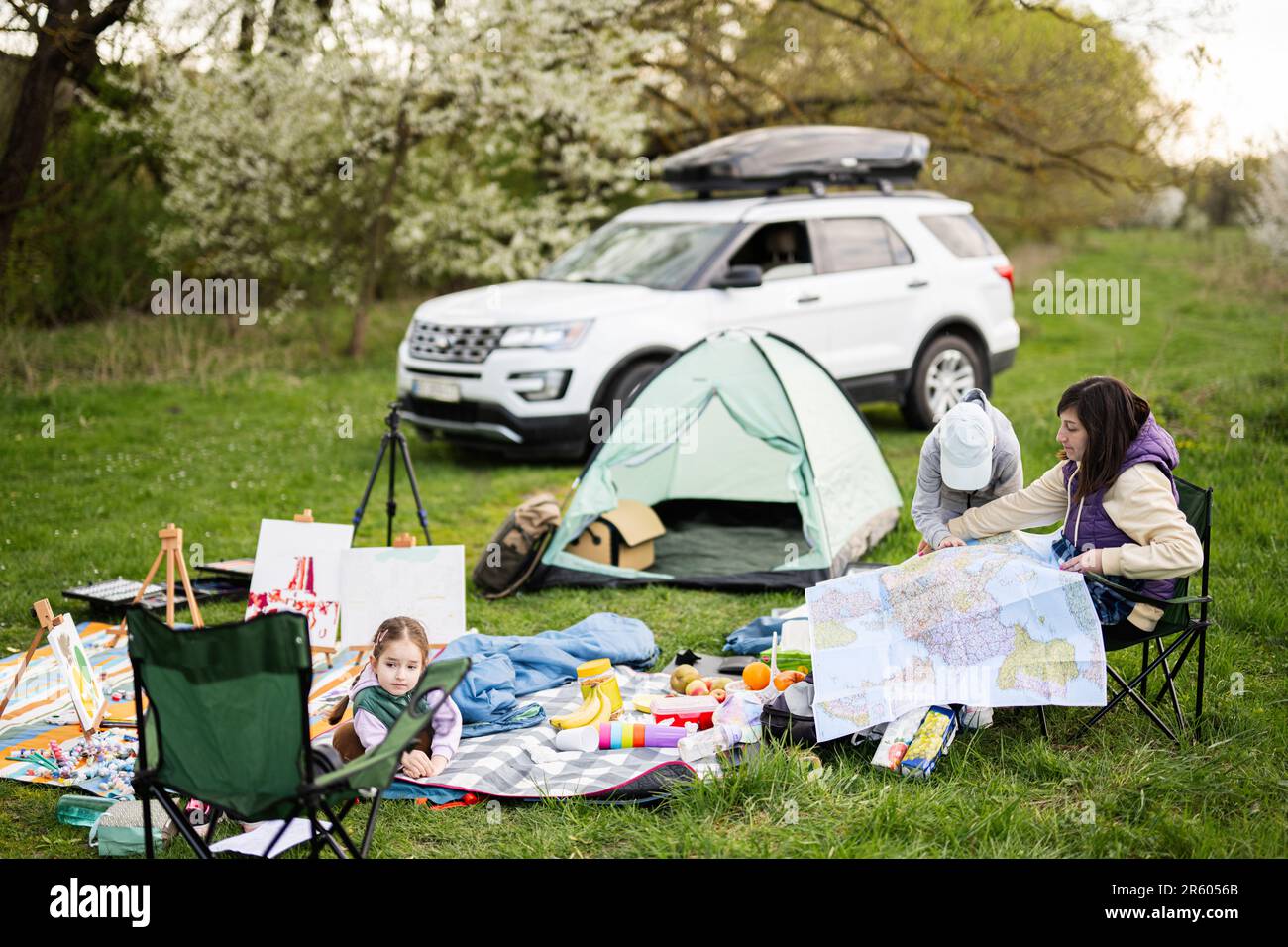 Mother hold europe map, with children sit on chair against car on picnic. Stock Photo
