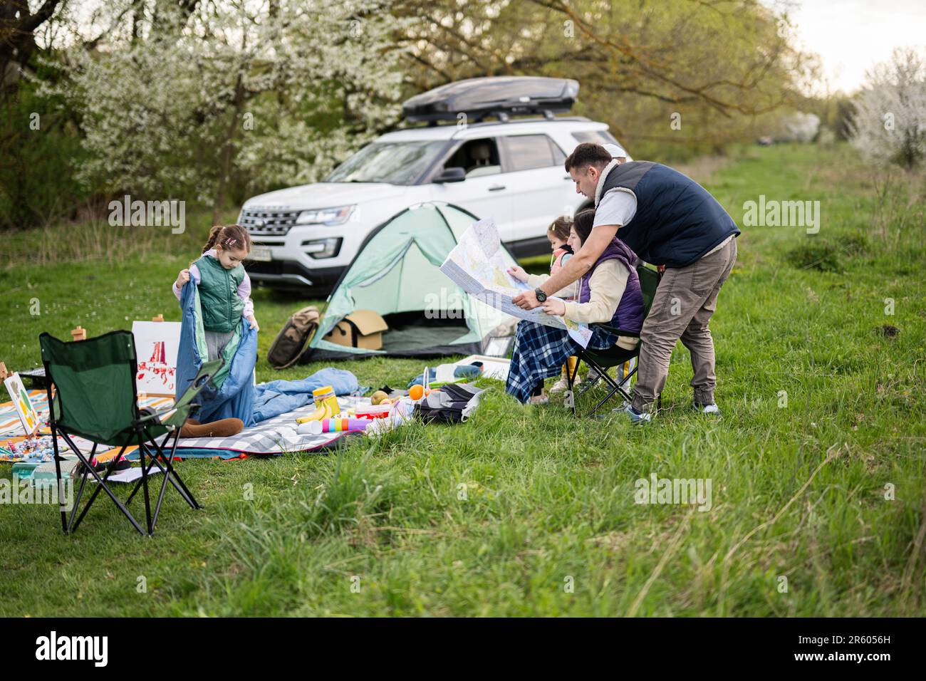 Family look at europe map, with children sit on chair against car on picnic. Stock Photo