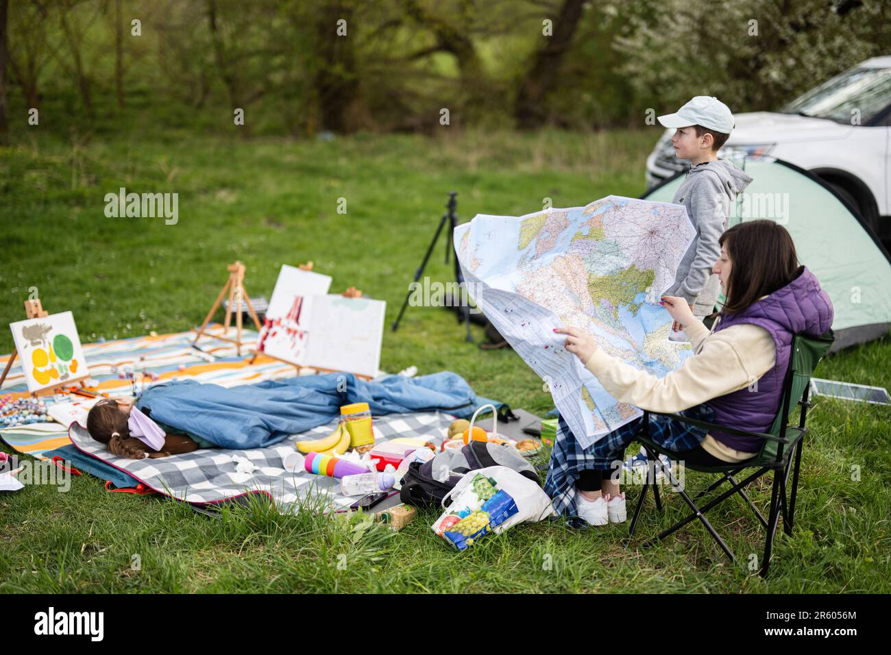Mother hold europe map, with children sit on chair against car on picnic. Stock Photo