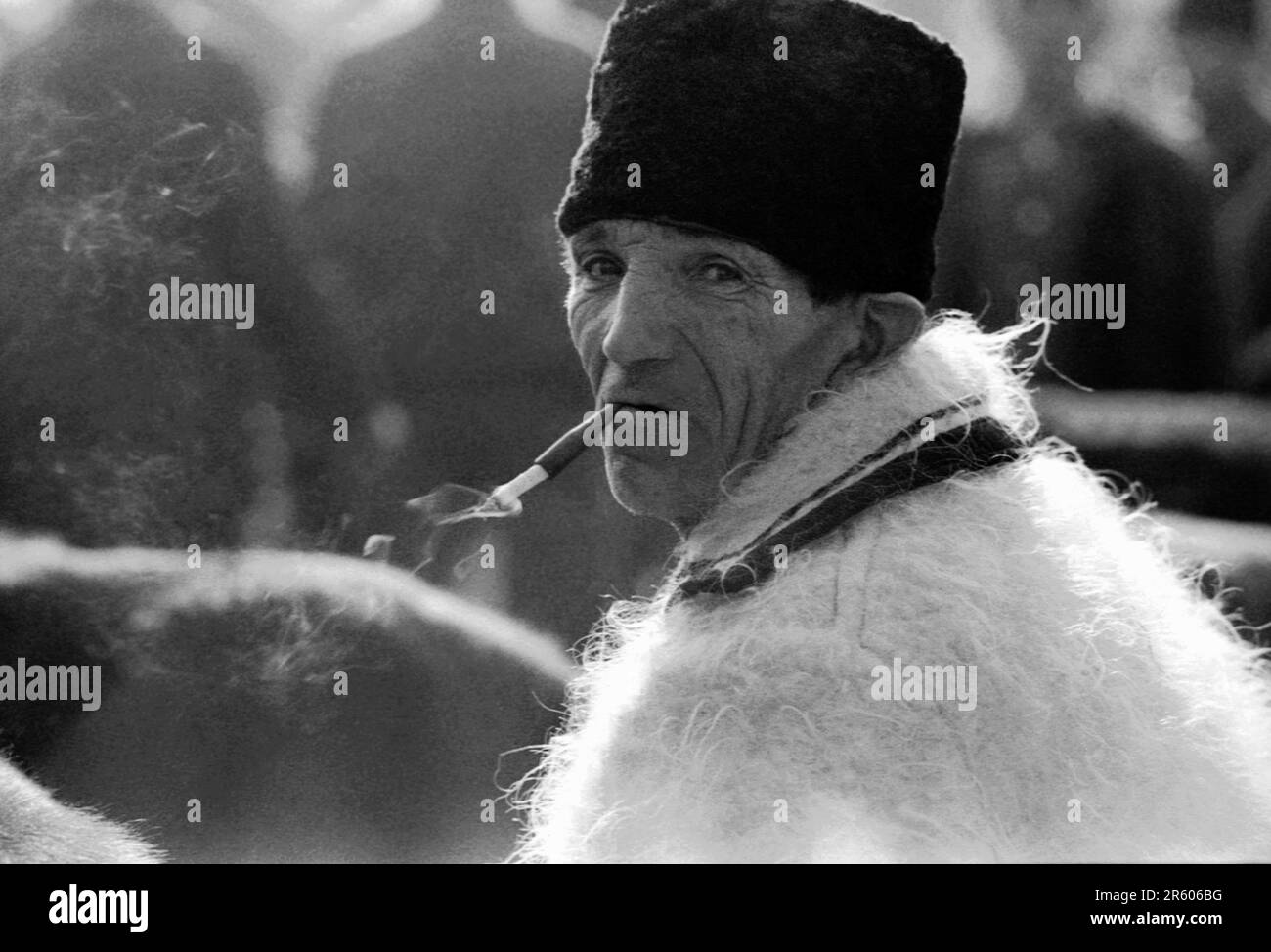 Maramures, Romania, approx. 1976. Local man in traditional woolen hat and coat, smoking a cigarette with a disposable filter. Stock Photo