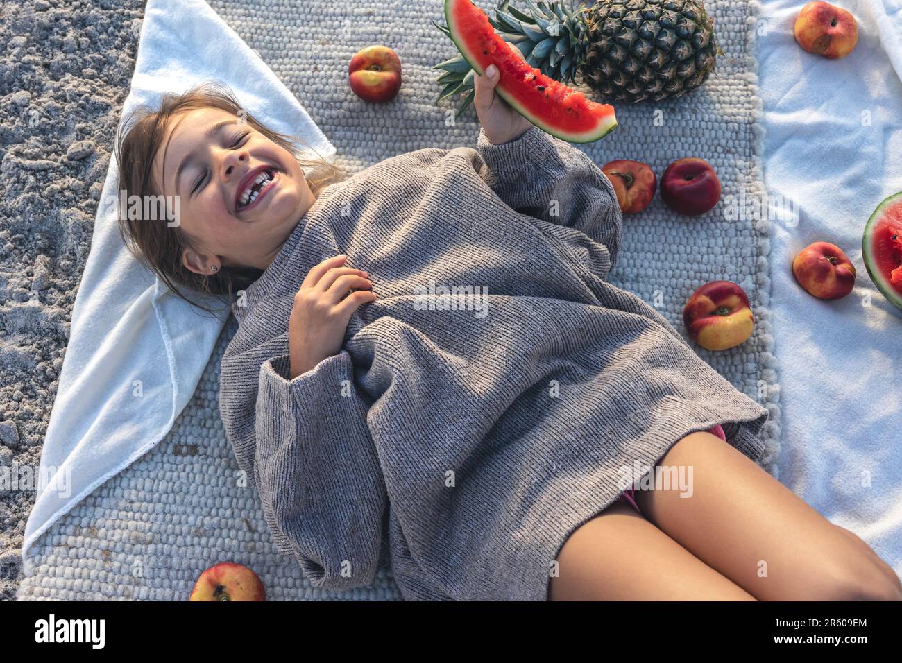 Little girl eats fruit lying on a blanket on the beach Stock Photo Alamy