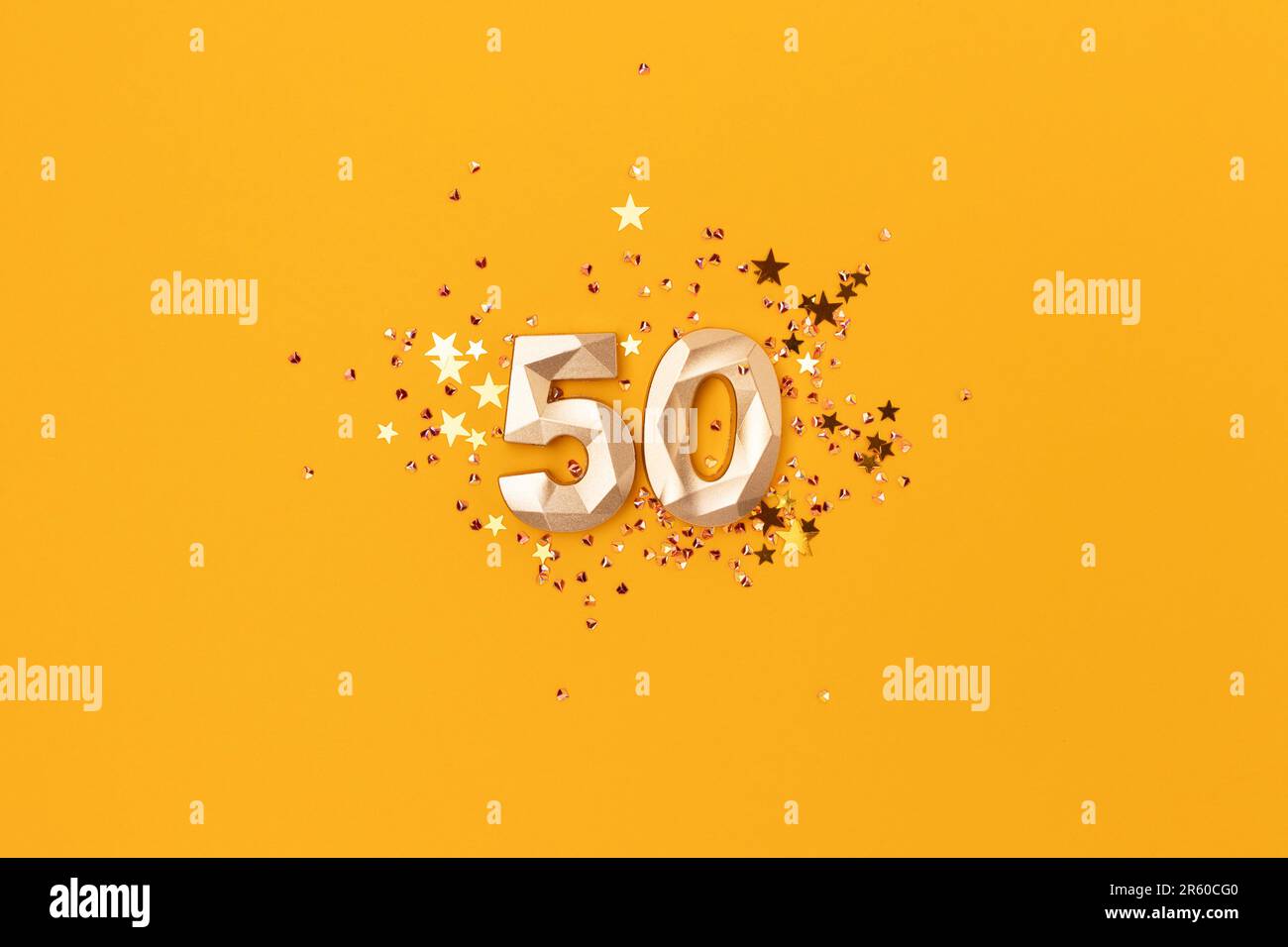 Gold colored number 50 and stars confetti on a yellow background. Festive compisition. Stock Photo
