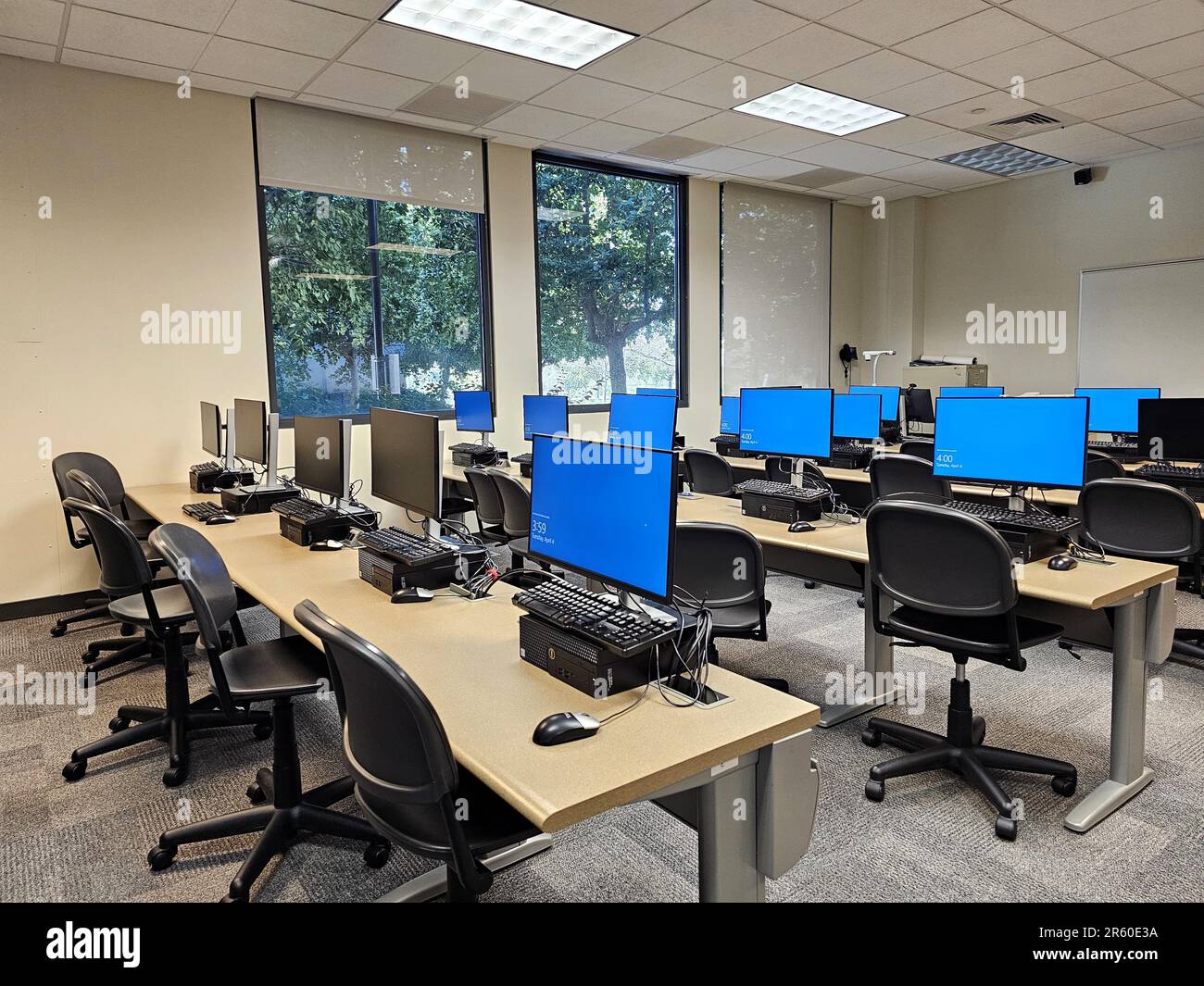 A modern classroom with computer monitors situated on desks. Stock Photo