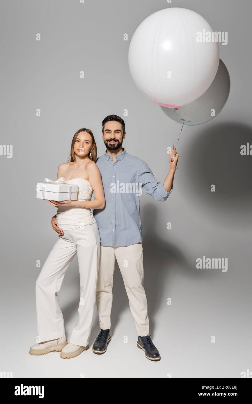 Hugging Balloons Full length of positive man holding festive balloons and hugging trendy ...
