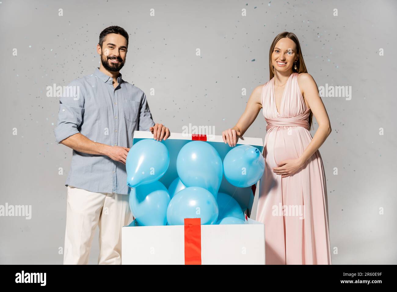 Positive pregnant woman in elegant dress opening bog gift box with