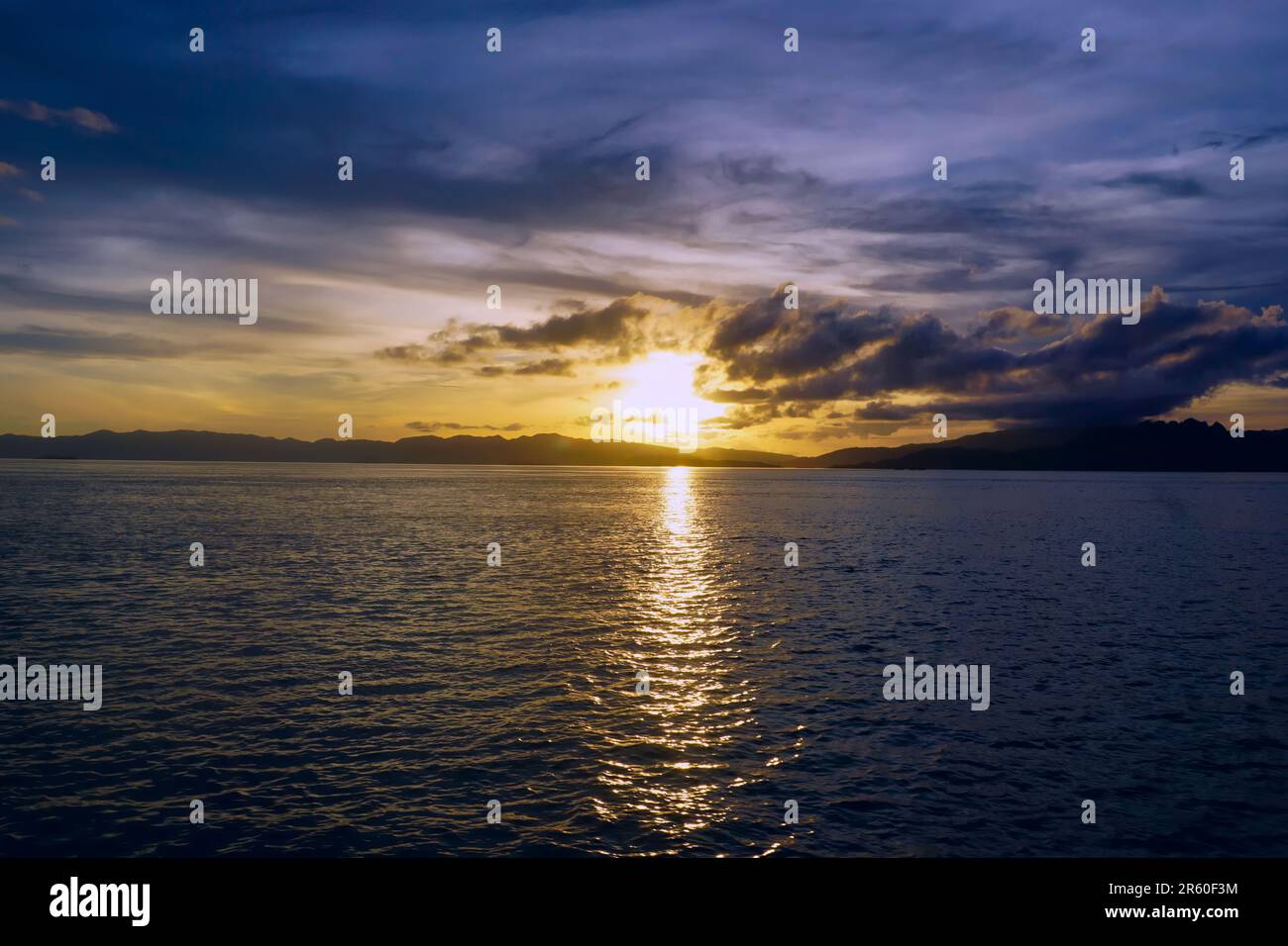Sunset over the sea in Komodo National Park, Indonesia, sun reflects in sea, clouds on the horizon Stock Photo