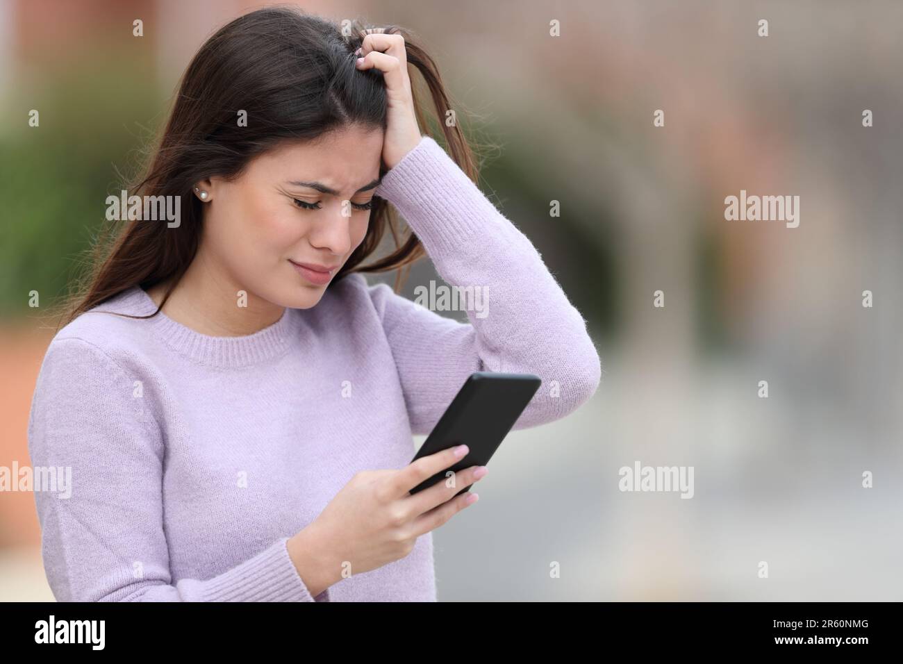 Sad teen complaining reading smart phone text standing in the street Stock Photo