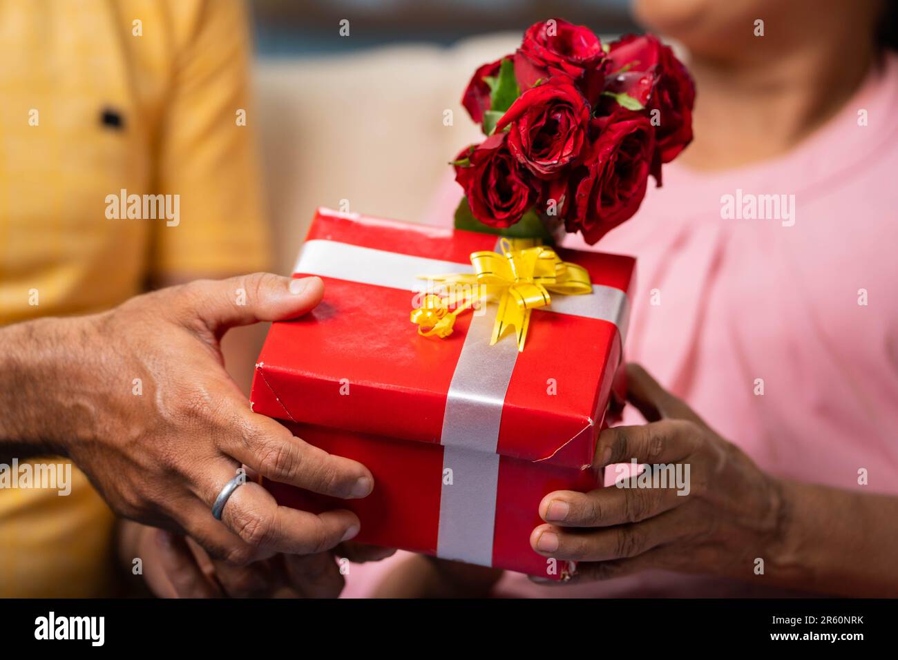 Close up shot of son hands giving gift with red roses to mother at home - concept of mother's day, family relationship and love moment. Stock Photo
