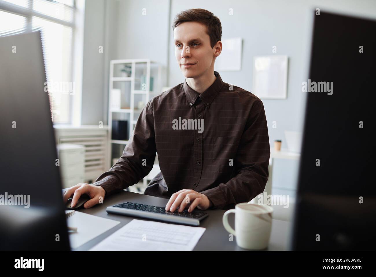 Portrait of smiling young man using computer in clean office workplace, copy space Stock Photo