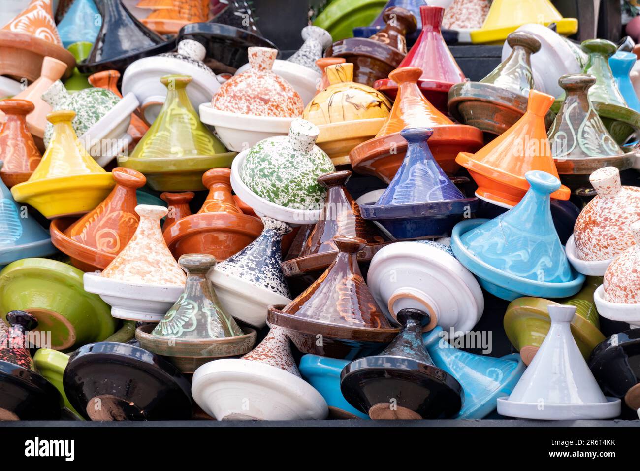 Assorted colourfully painted and glazed Moroccan tagines or tajines for sale in a souk or market in Morocco. the tagines are piled high on the stall Stock Photo