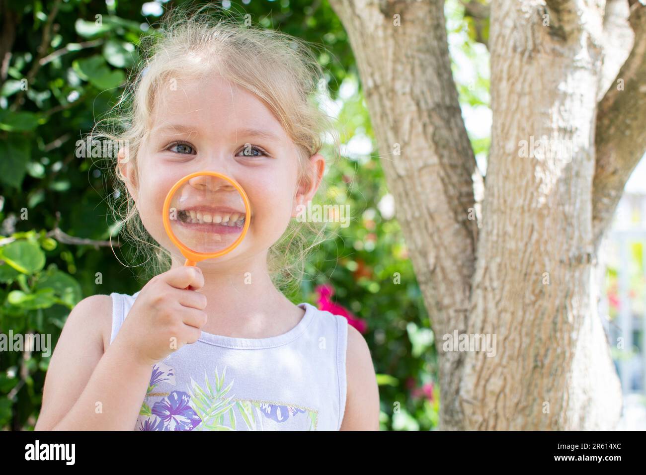 Smiling Caucasian preschool girl with magnifying glass. Happy childhood