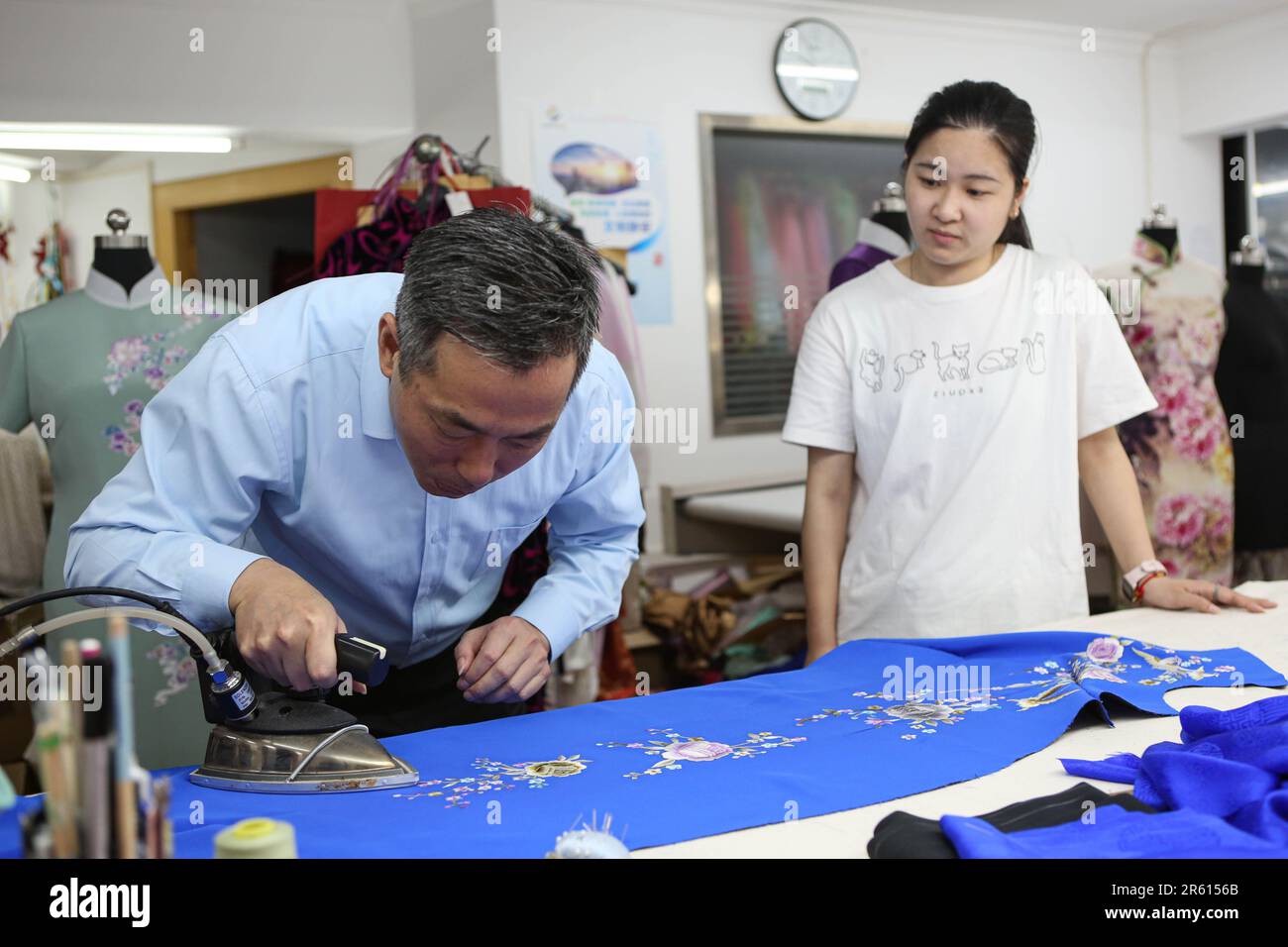 (230606) -- SHANGHAI, June 6, 2023 (Xinhua) -- Jiang Manzong (L) irons a piece of semi-finished cheongsam at a training institute for Longfeng Cheongsam in Shanghai, east China, May 31, 2023. Cheongsam, or Qipao, is a traditional wearing of Chinese women which takes inspiration from the ethnic clothing of Manchu people. Evolving with the time, it nowadays represents a new fashion for Chinese women who value the tradition and elegance.  As a representative of Shanghai-style cheongsam which emphasizes the beauty of woman's curve, the Longfeng cheongsam traces back to the reign of China's Qing Dy Stock Photo