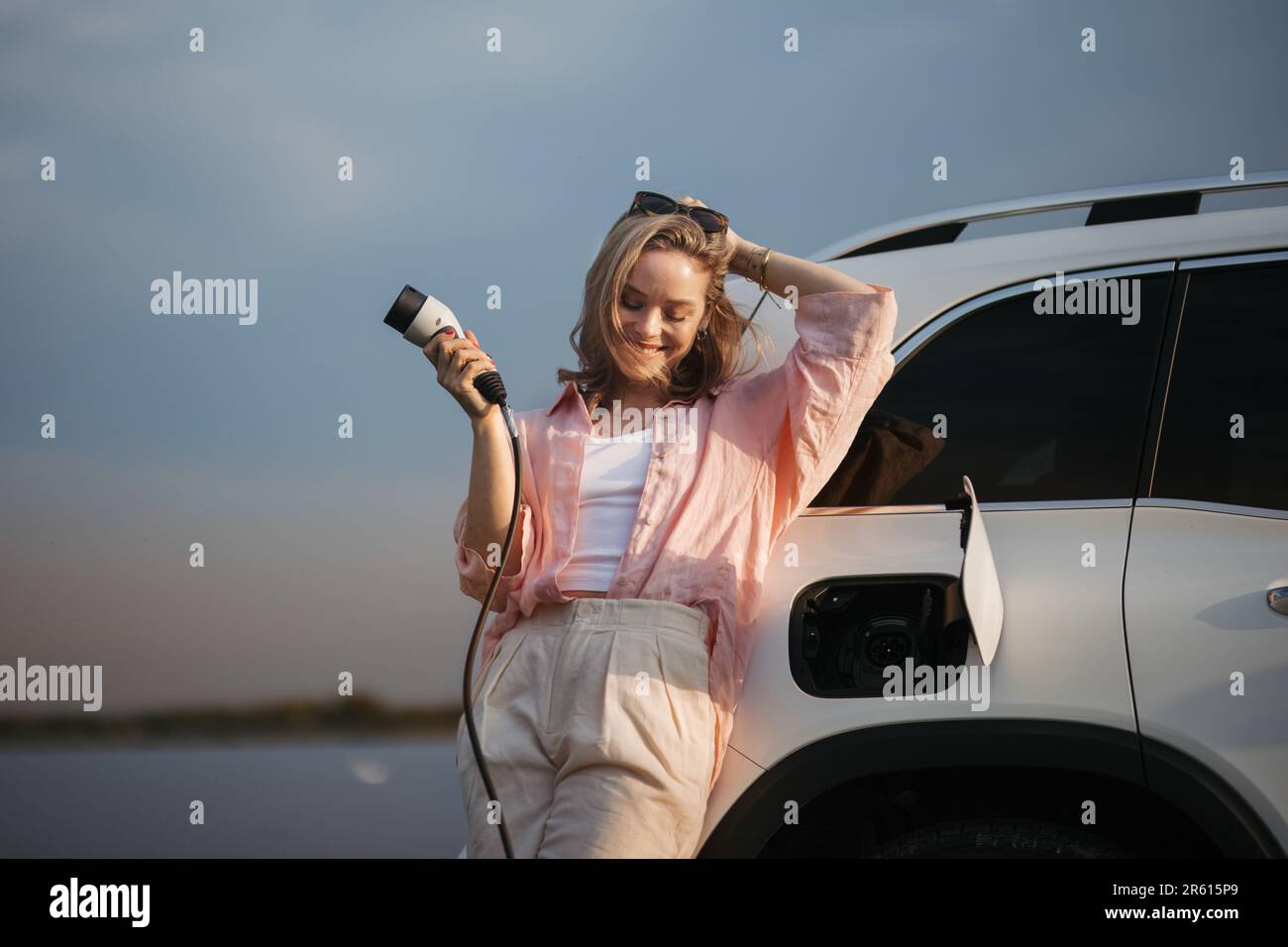 Young woman holding power supply cable from her electric car, prepared for charging it sustainable and economic transportation concept. Stock Photo