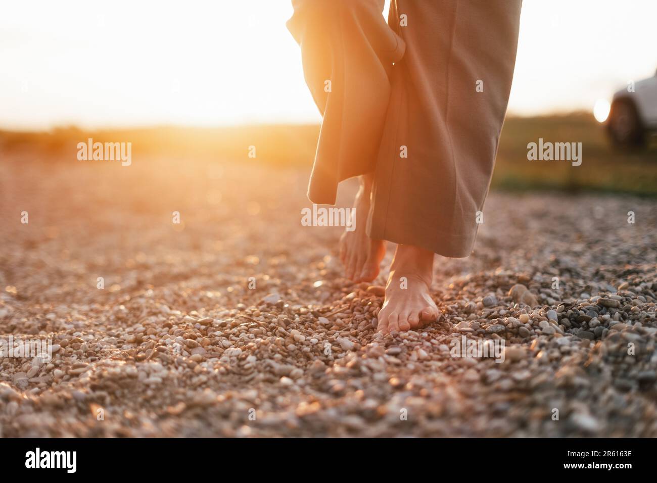 Close up of womans barefoot feet walking on rock beach. Stock Photo