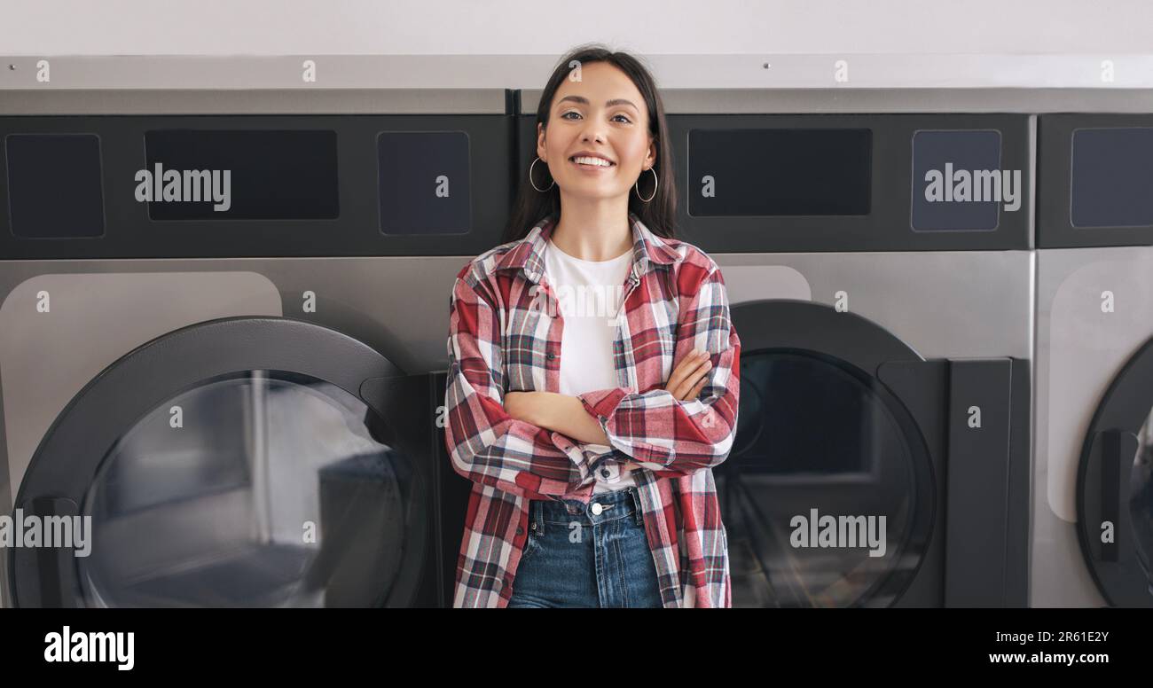 Happy Young Woman Posing Near Washing Machines At Public Laundry Stock Photo