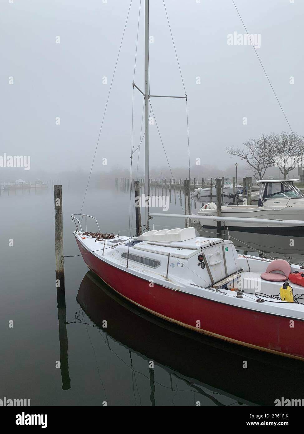 Boats are tied to wooden pylons at a dock on a foggy and stormy day near the water Stock Photo