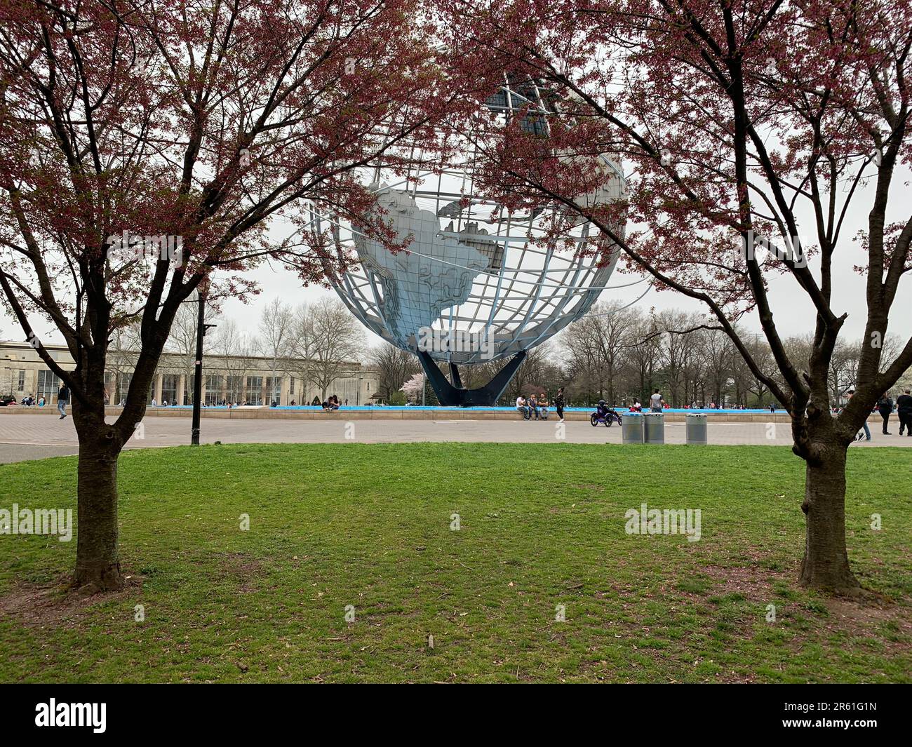 People gather around the Unisphere, a landmark from the 1964 New York Worlds Fair, surrounded by blooming cherry blossom trees in Queens New York City Stock Photo