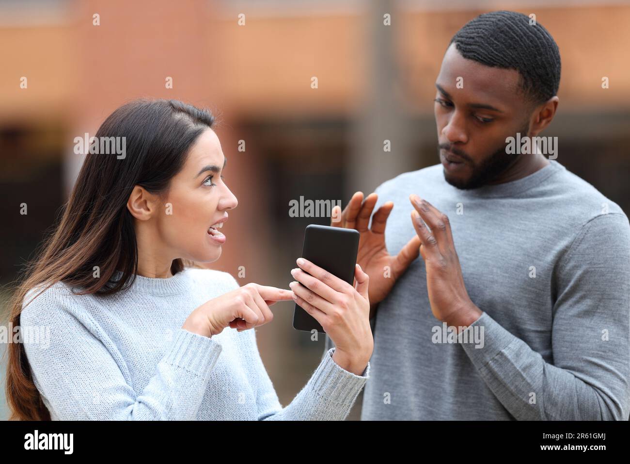 Angry woman scolding a shocked man showing cell phone content in the street Stock Photo