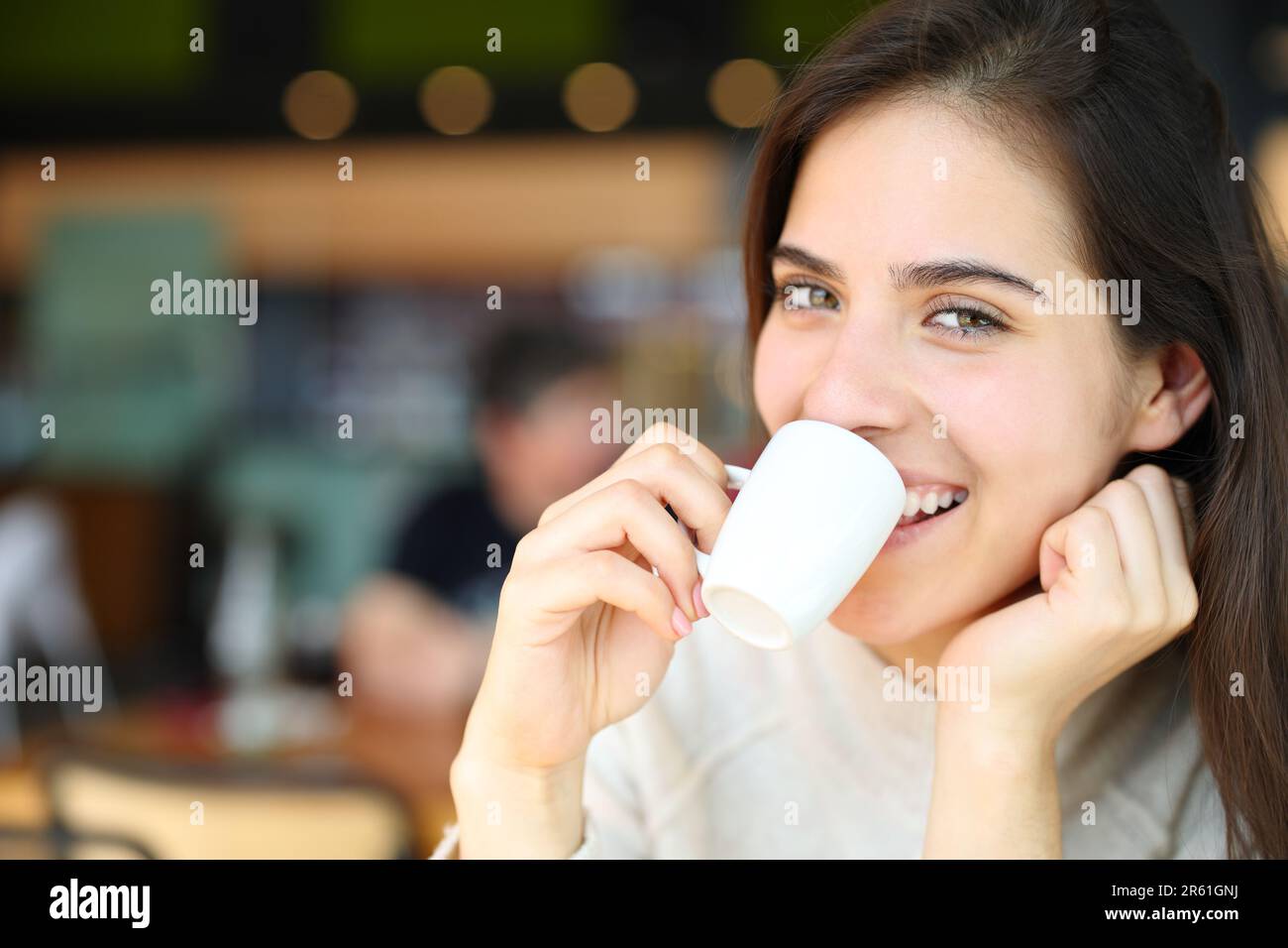 Happy woman drinking coffee in a bar looks at you smiling Stock Photo