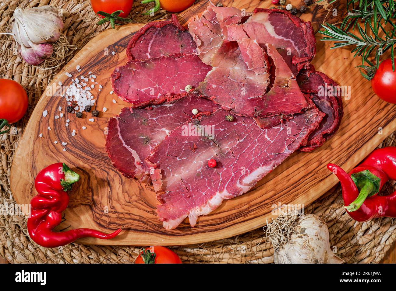 Cured meat, bacon or Turkish pastirma on cutting board with vegetables and spices, meat dish traditional Turkish food for sunday breakfast Stock Photo