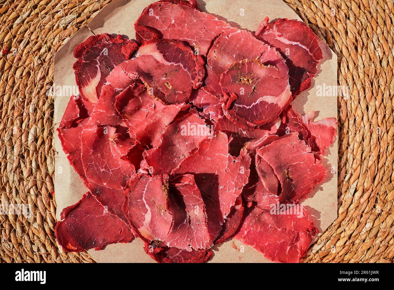Turkish bacon, pastrami or kayseri pastirma. Fresh sliced pastrami on a paper lining, top view. Stock Photo