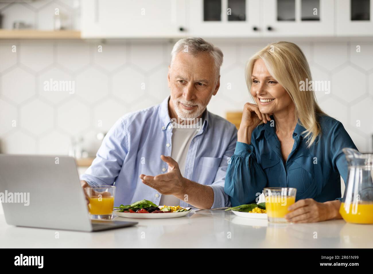 Smiling senior couple using laptop in kitchen while having breakfast together Stock Photo