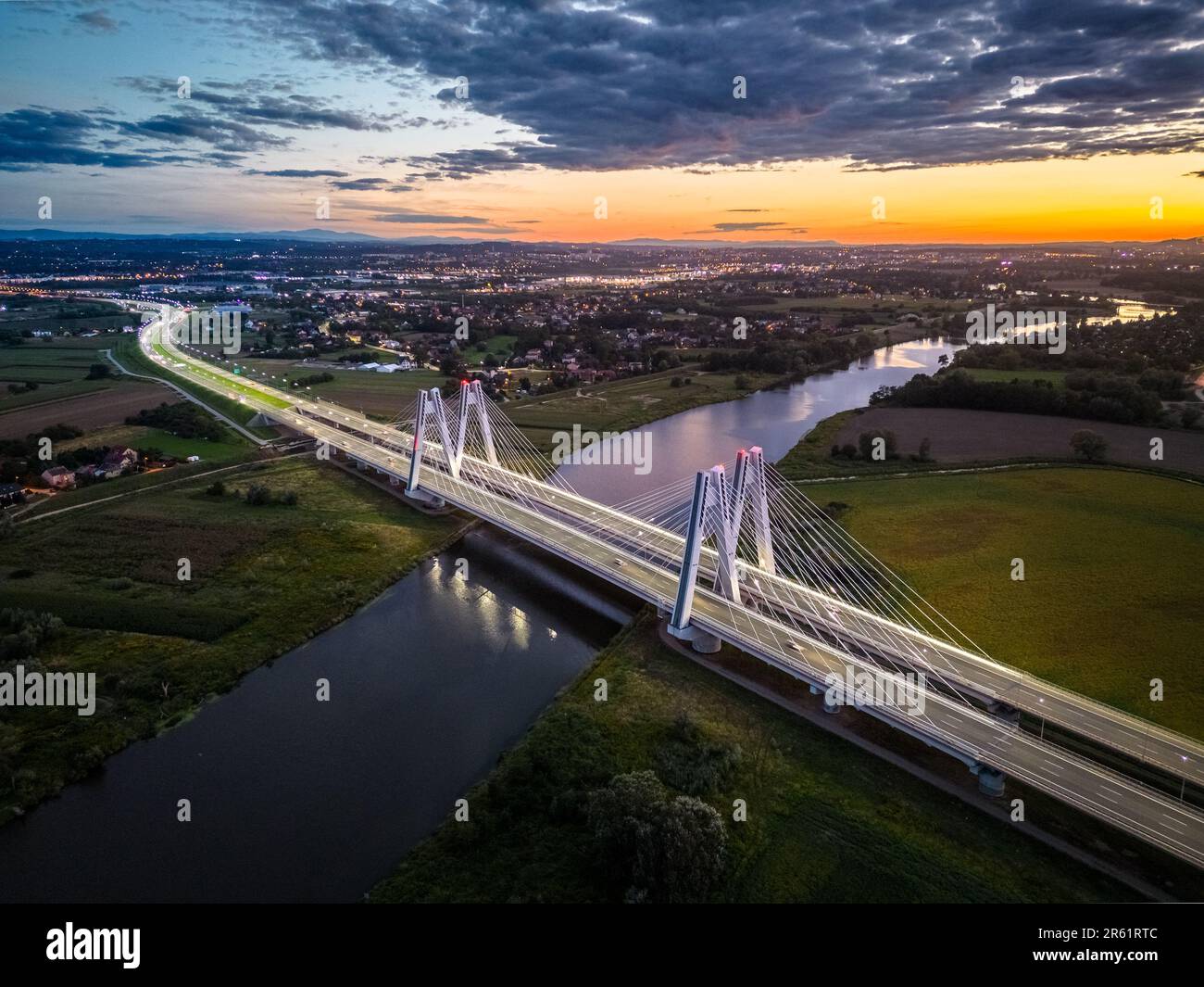An aerial view of a long bridge spanning a wide river at sunset in a ...