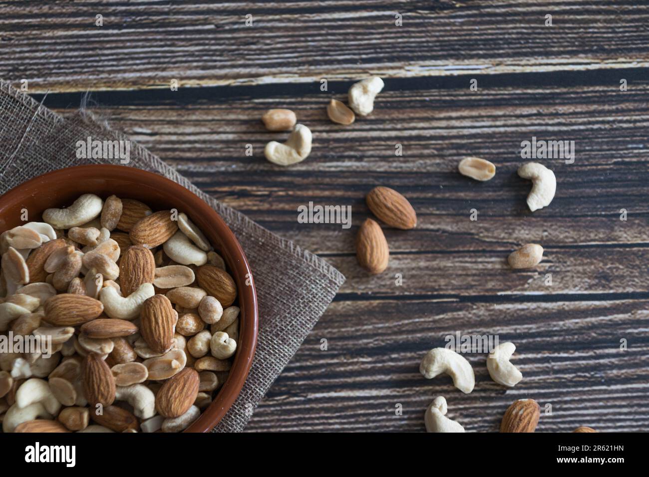A shallow bowl filled with assorted nuts is placed on a wooden table Stock Photo
