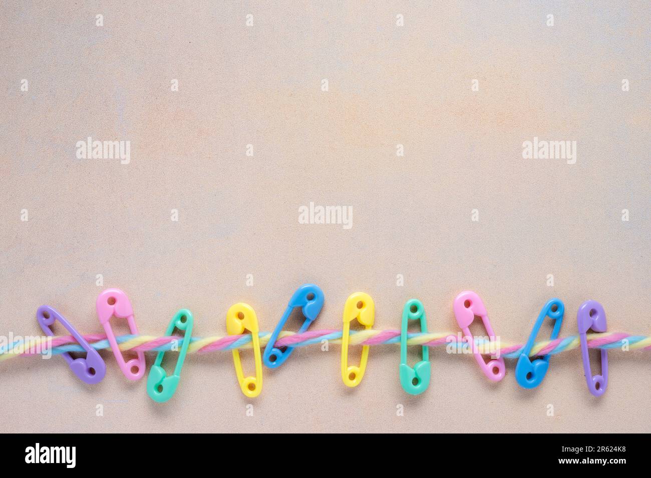colorful baby concept flat lay with bright plastic diaper pins on a multi colored fuzzy yarn line with mottled yellow background Stock Photo